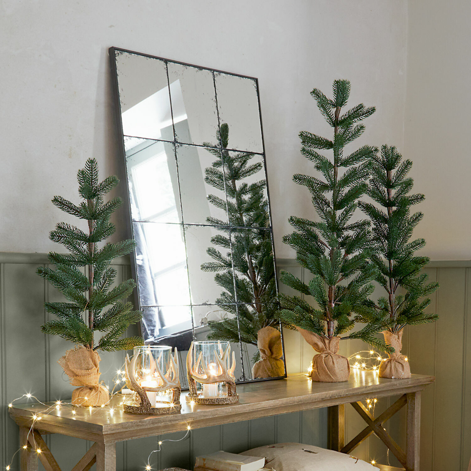 Set de 3 árboles decorativos Merpins Pequeños árboles de Navidad artificiales decorativos en saco de yute sobre mesa de madera con luces LED y espejo