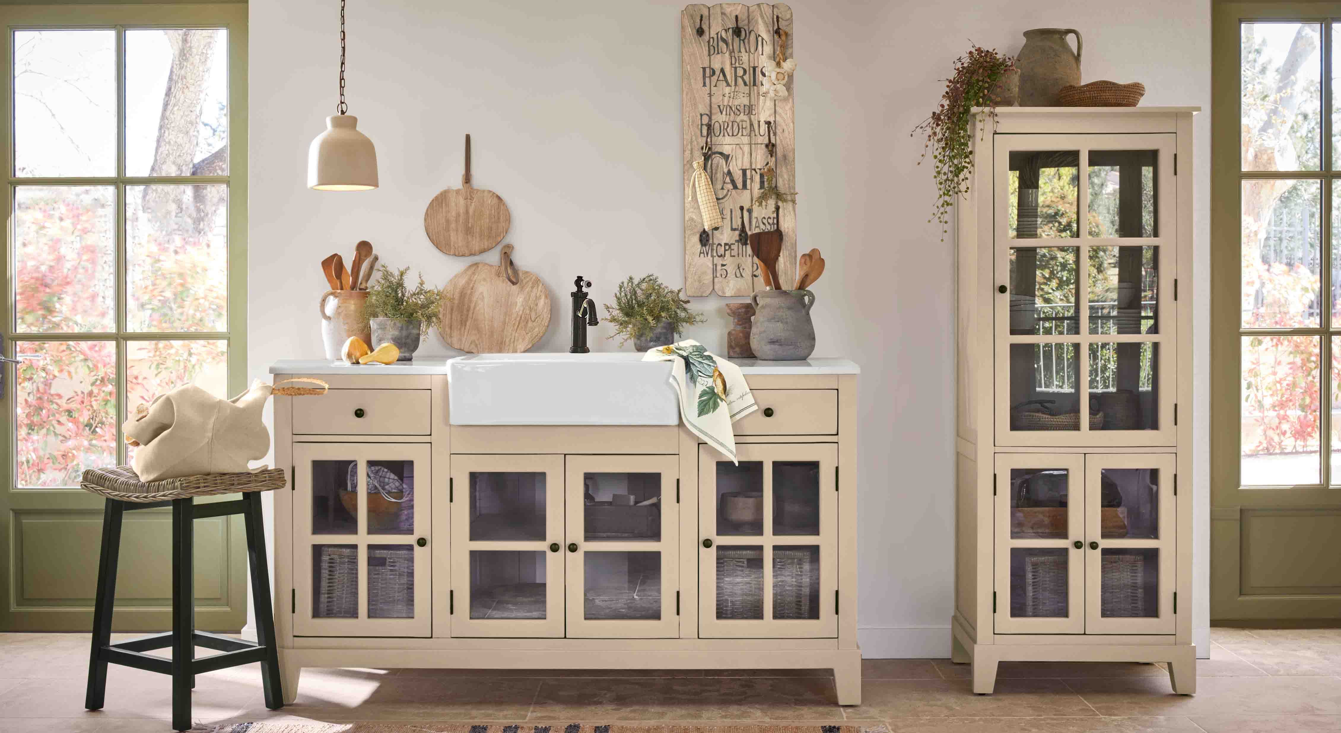 Cocina rústica con armarios beige con puertas de cristal y fregadero cerámico blanco, decoraciones de madera y plantas