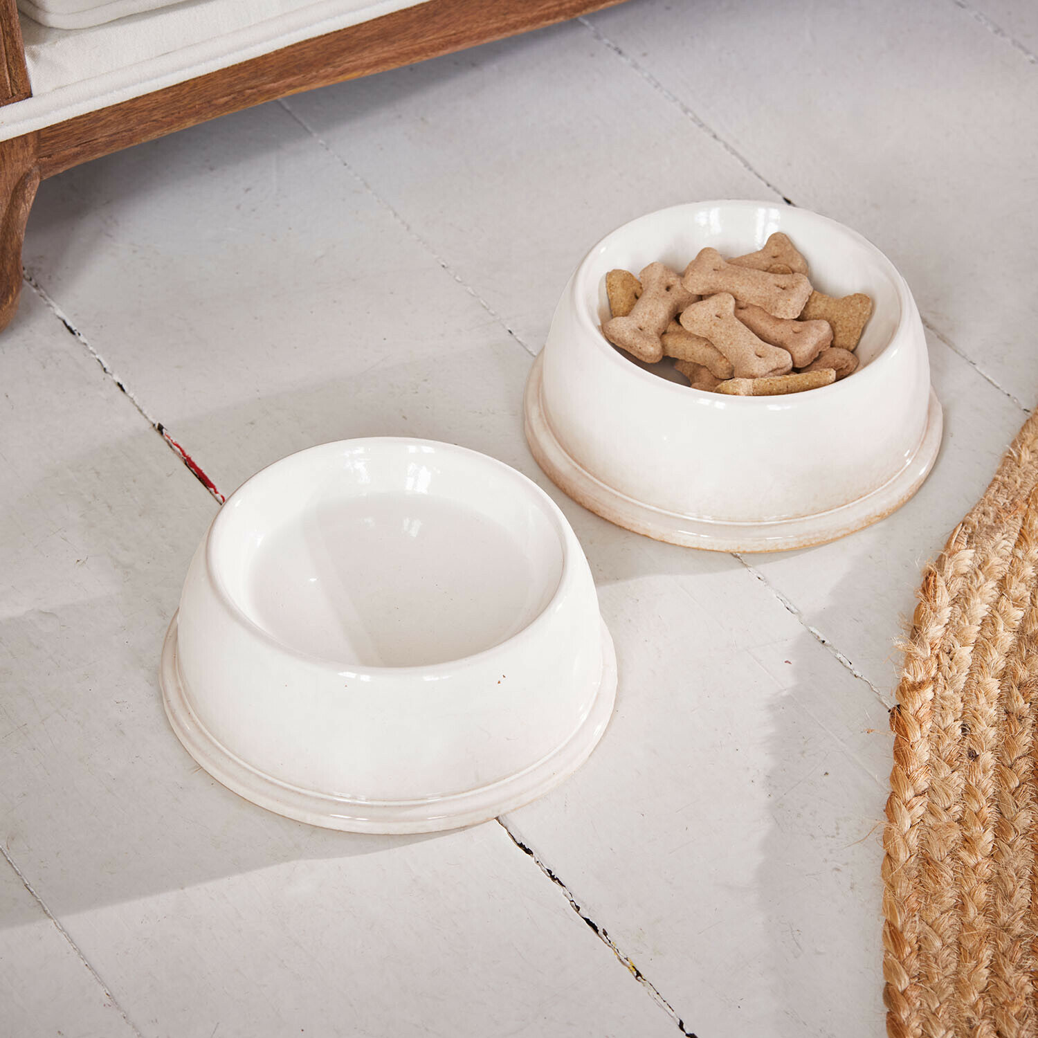 Set de 2 comederos Kireva Dos cuencos blancos de cerámica para perro, uno con galletas en forma de hueso y otro vacío