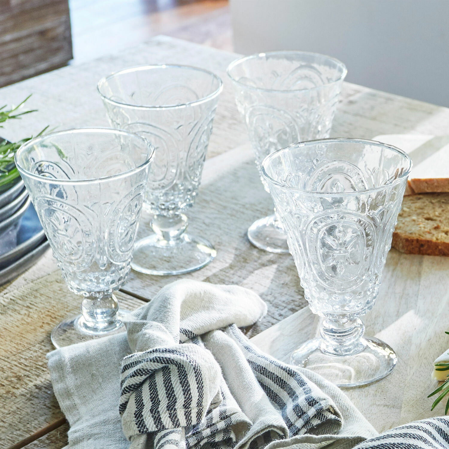 Conjunto de cuatro vasos transparentes con diseño decorativo sobre mesa de madera con tela y pan