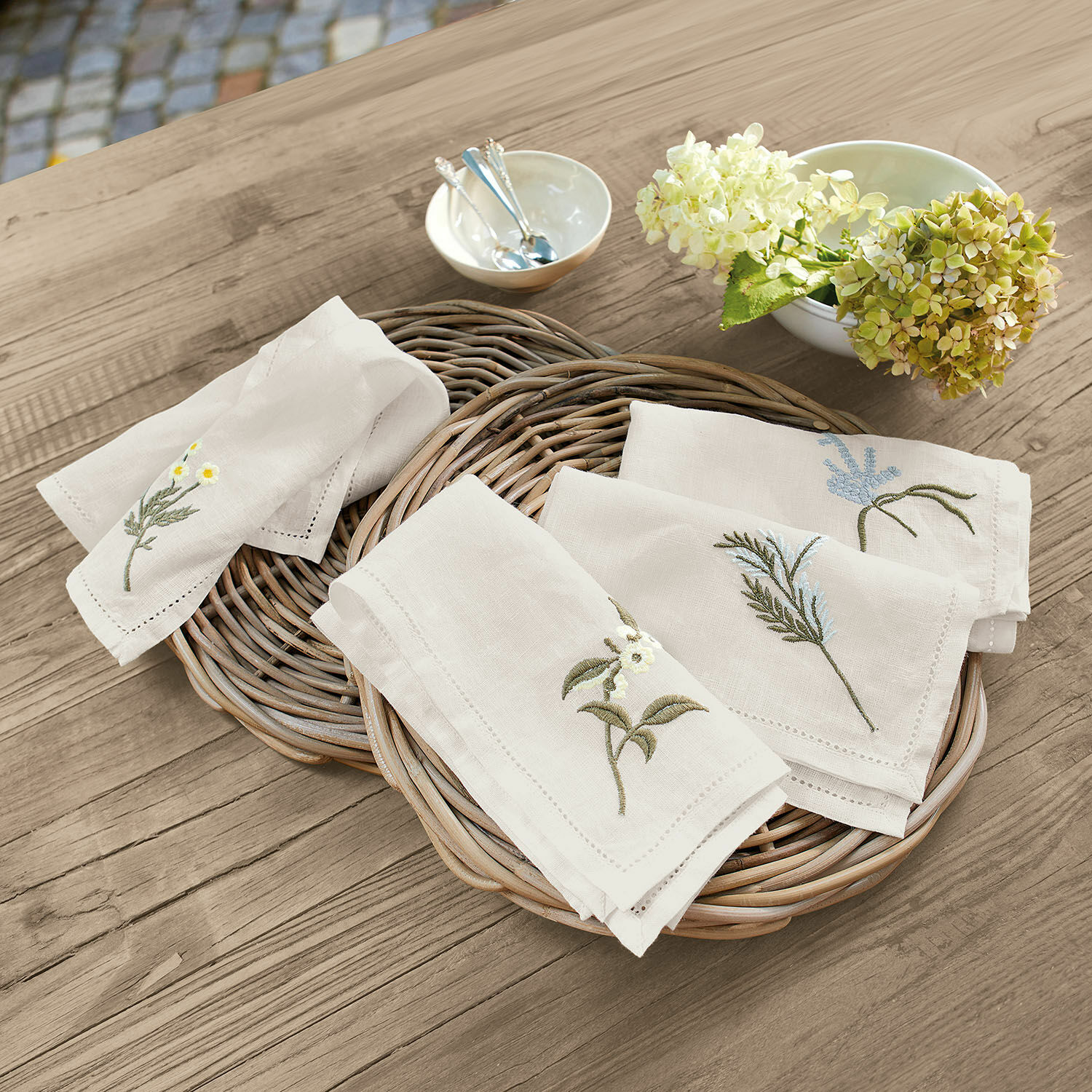 Set de 4 servilletas Lentilly Servilletas de lino natural con bordado floral sobre cesta de mimbre en mesa de madera