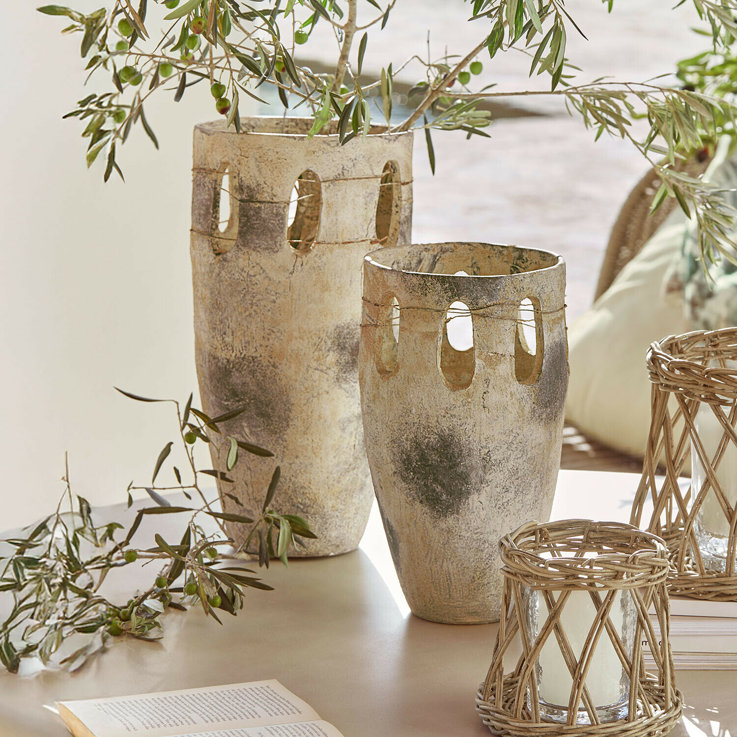 Set de 2 jarrones Delunas Dos jarrones decorativos de piedra beige grisácea con aberturas y ramas de olivo sobre una mesa