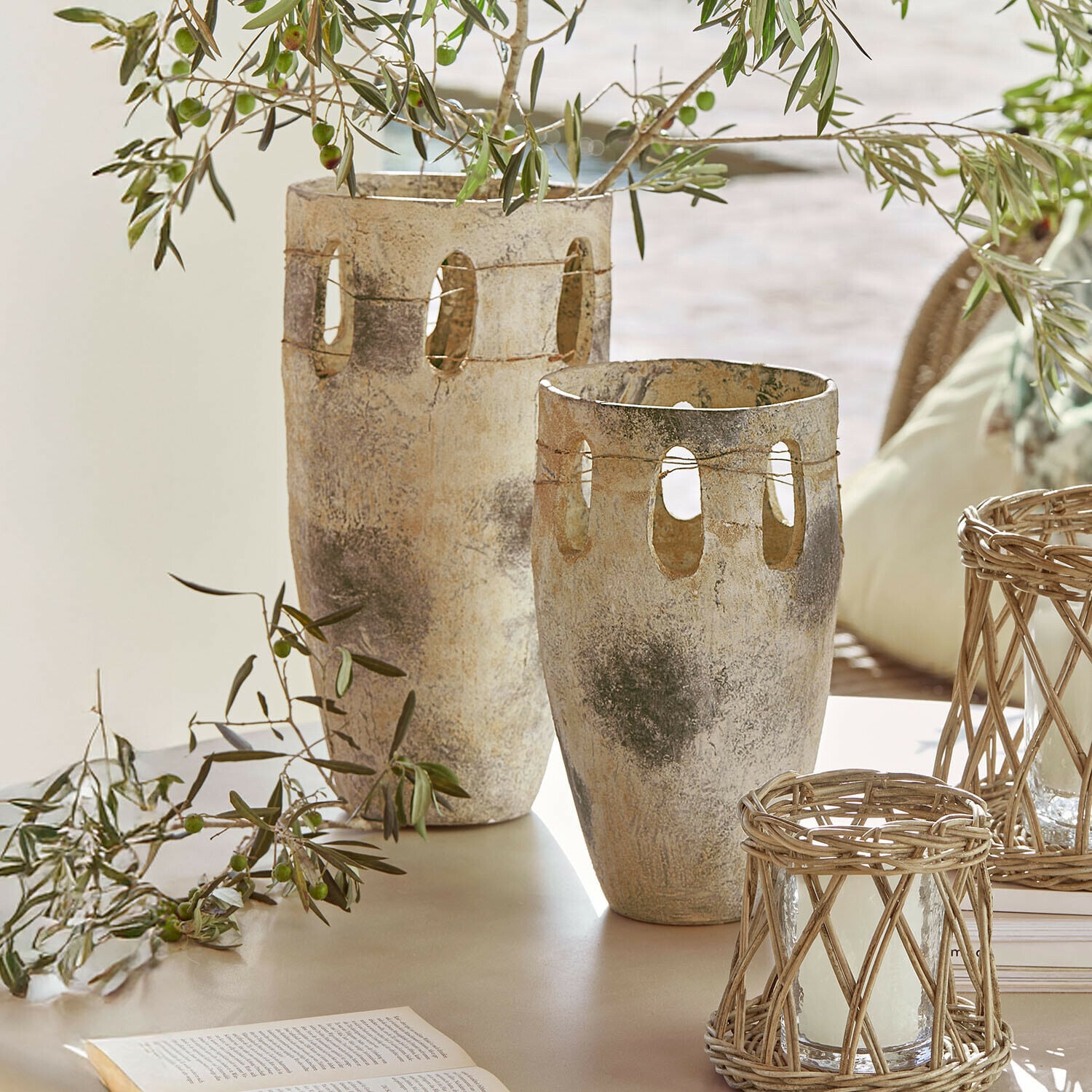 Set de 2 jarrones Delunas Dos jarrones decorativos de piedra beige grisácea con aberturas y ramas de olivo sobre una mesa