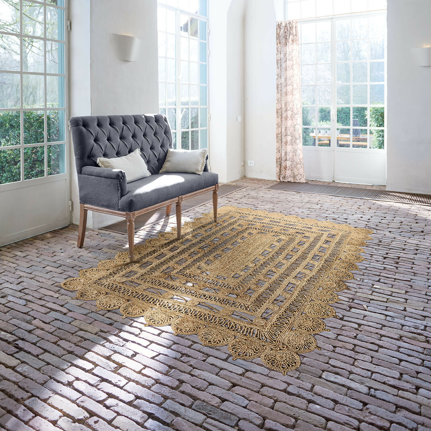 Alfombra Livadia Sofá gris capitoné con patas de madera en habitación luminosa con alfombra de yute sobre suelo de ladrillo