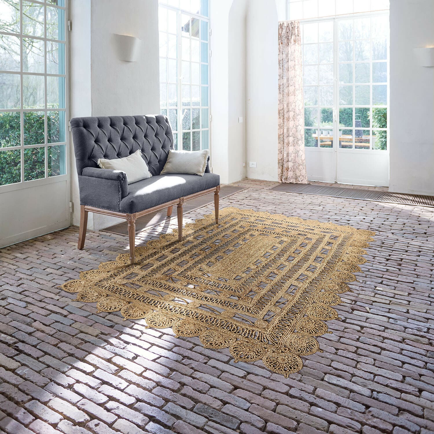 Alfombra Livadia Sofá gris capitoné con patas de madera en habitación luminosa con alfombra de yute sobre suelo de ladrillo