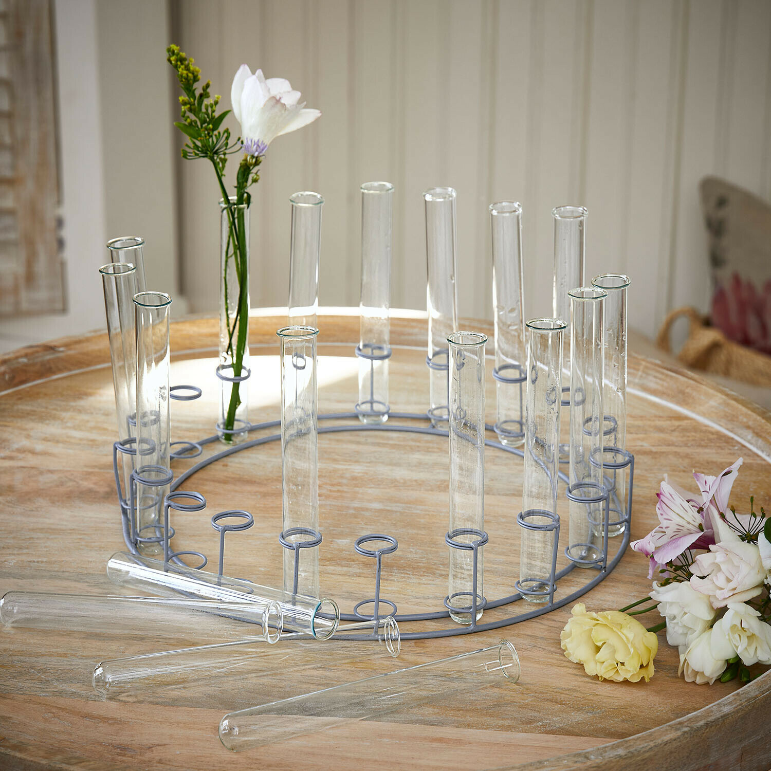 Soporte redondo de metal con tubos de vidrio transparentes para flores sobre mesa de madera clara