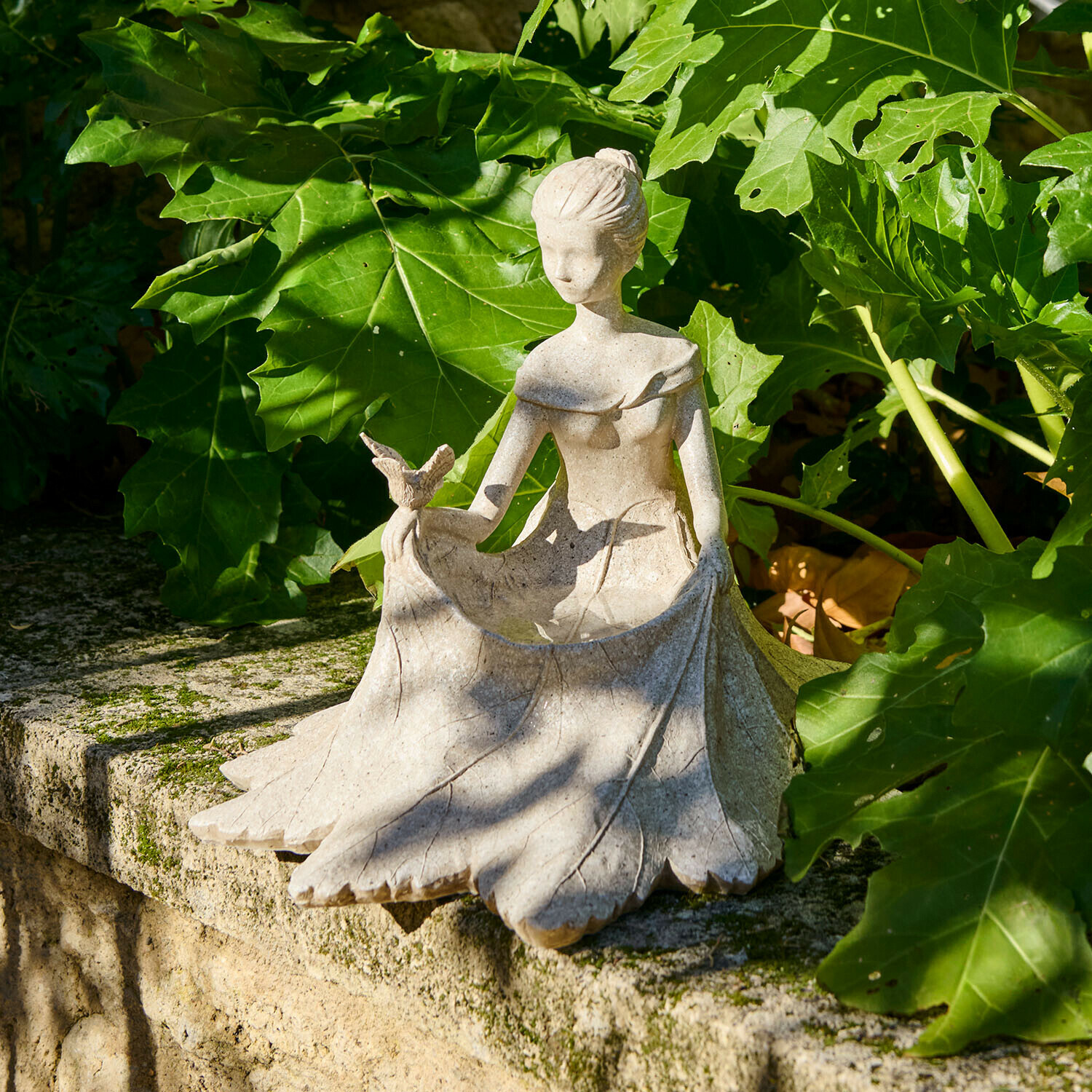 Figura decorativa Finnedra Figura de mujer de piedra con pájaro, decoración de jardín sobre muro de piedra rodeada de hojas verdes