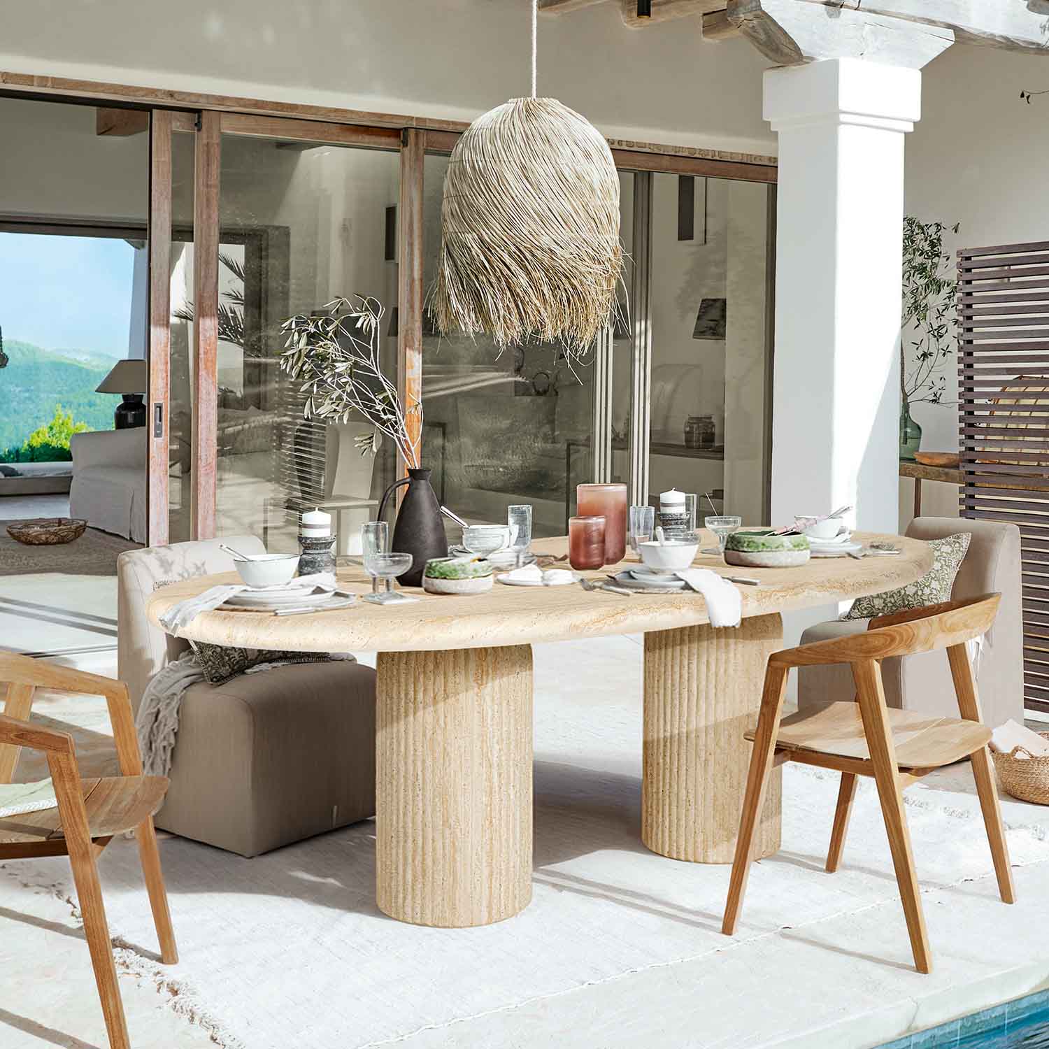 Mesa de comedor de piedra clara con patas cilíndricas, rodeada de sillas de madera y tapizadas en un espacio luminoso