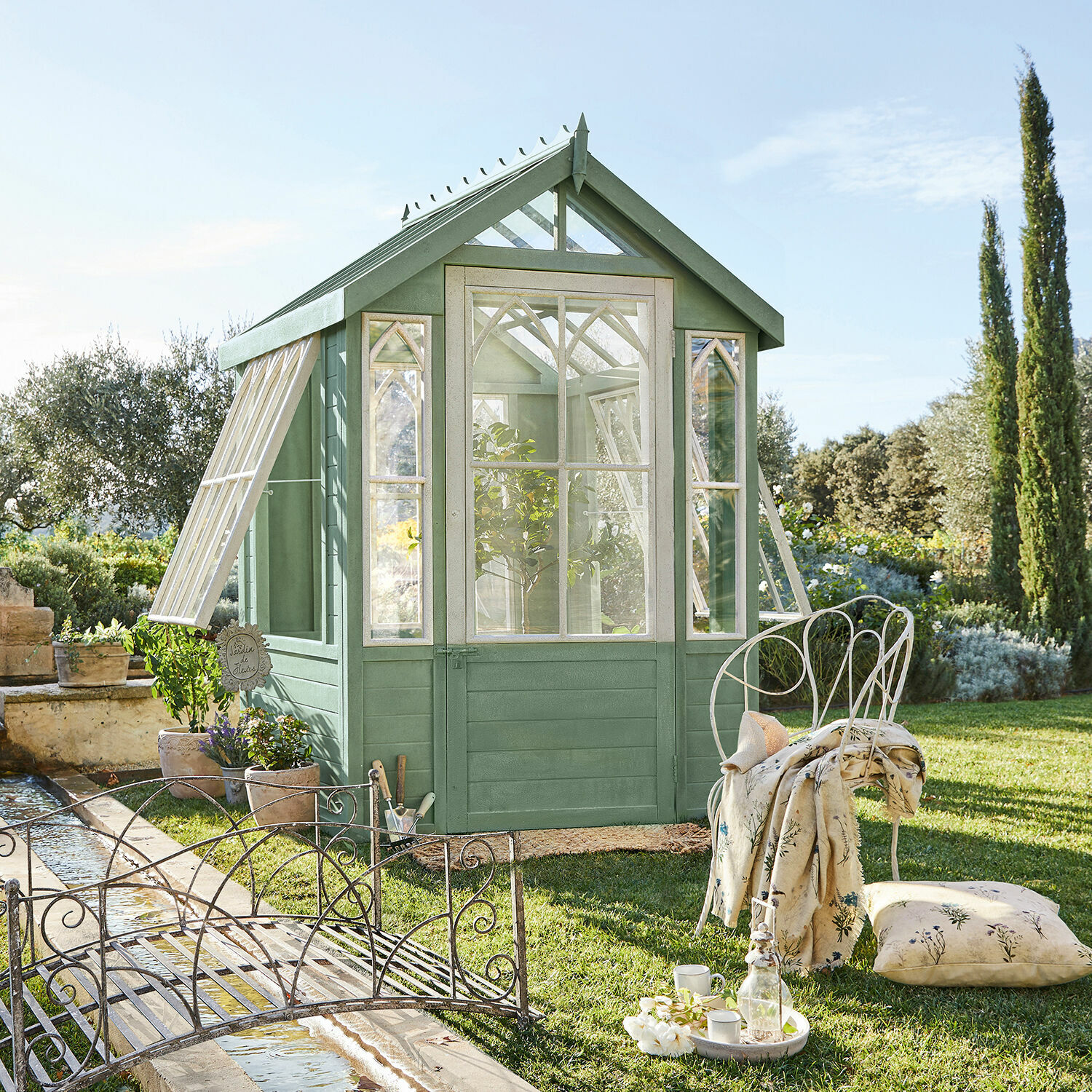Caseta de jardín Anyós Invernadero de jardín de madera verde con ventanas blancas y muebles de metal sobre césped