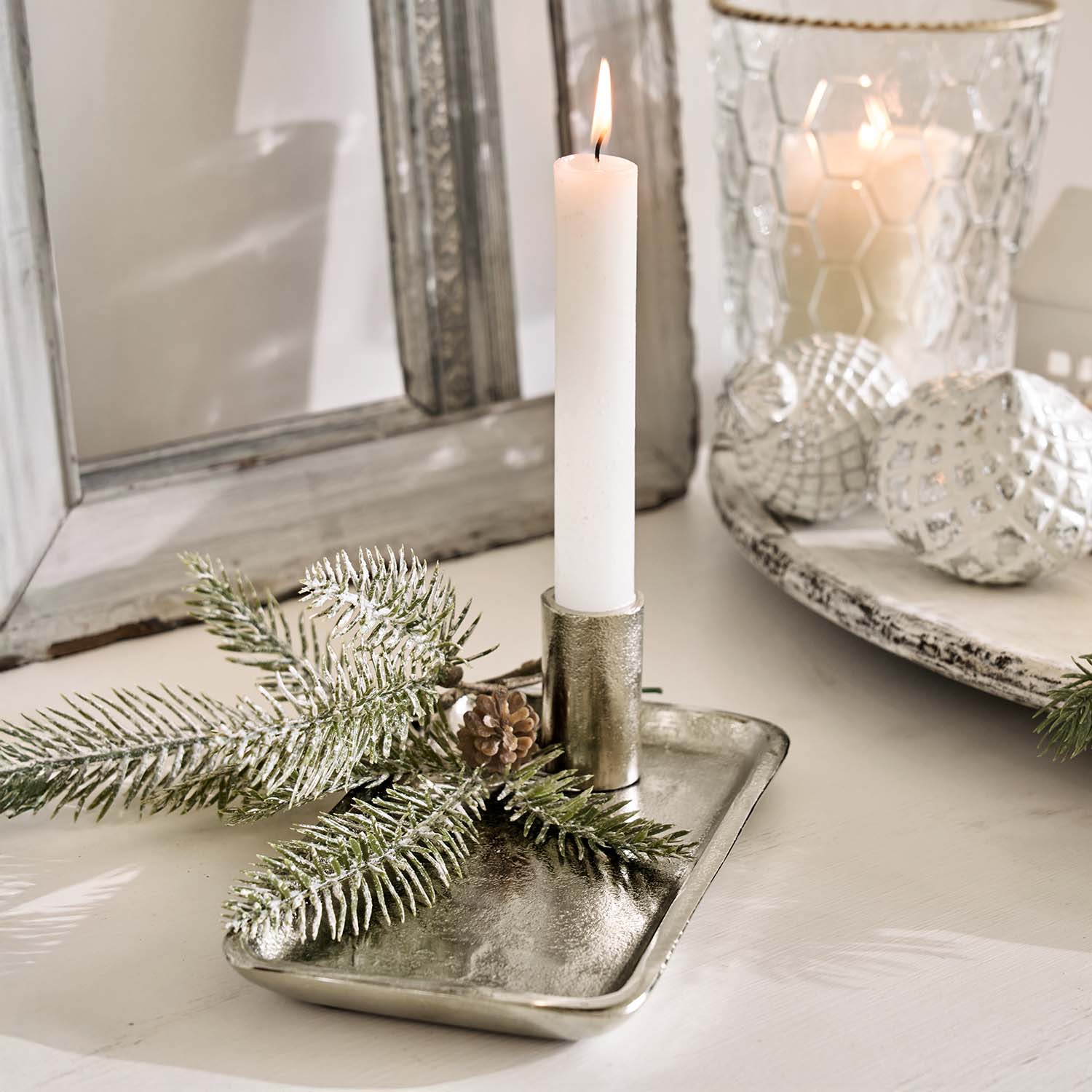 Portavelas metálico plateado con vela blanca y decoración de ramas de pino sobre mesa clara