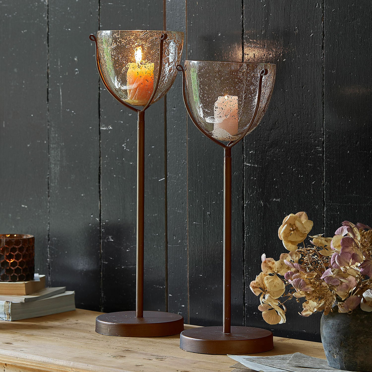 Set de 2 portavelas Piacello Dos candelabros de metal marrón con base redonda y vidrio con burbujas con velas encendidas