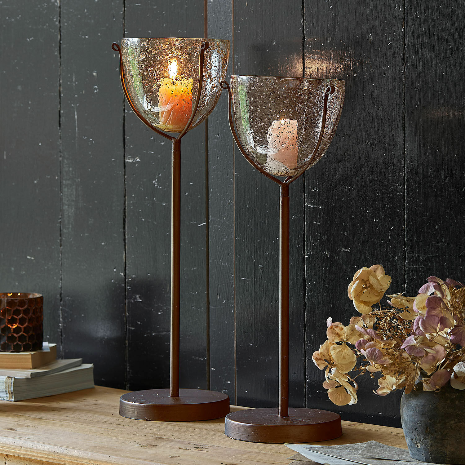 Set de 2 portavelas Piacello Dos candelabros de metal marrón con base redonda y vidrio con burbujas con velas encendidas