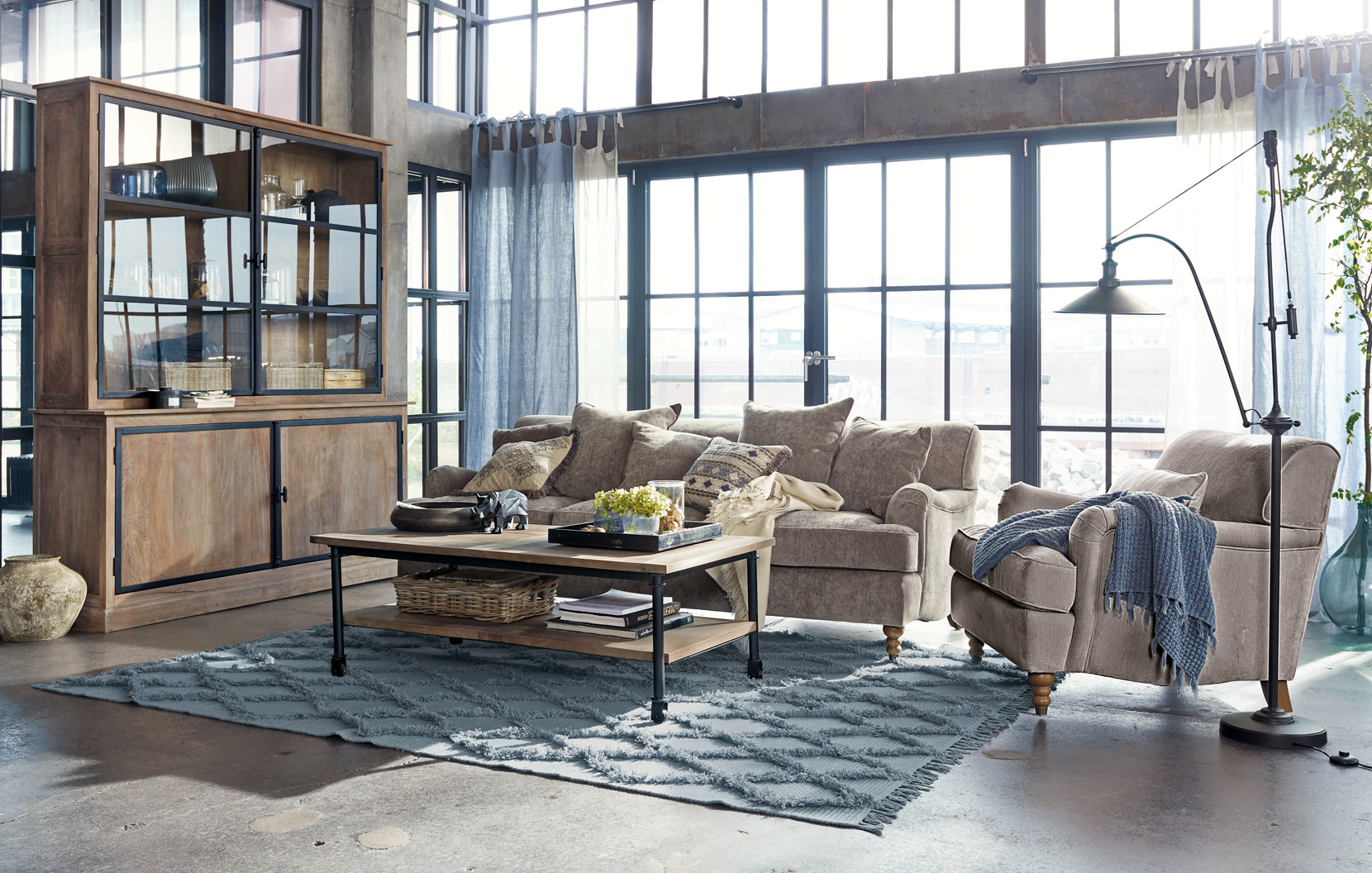 Acogedora sala de estilo loft con sofá beige, mueble de madera y alfombra azul sobre suelo de hormigón