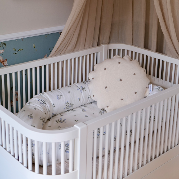 Cuna blanca para bebé con cojín suave y ropa de cama floral en tonos pastel