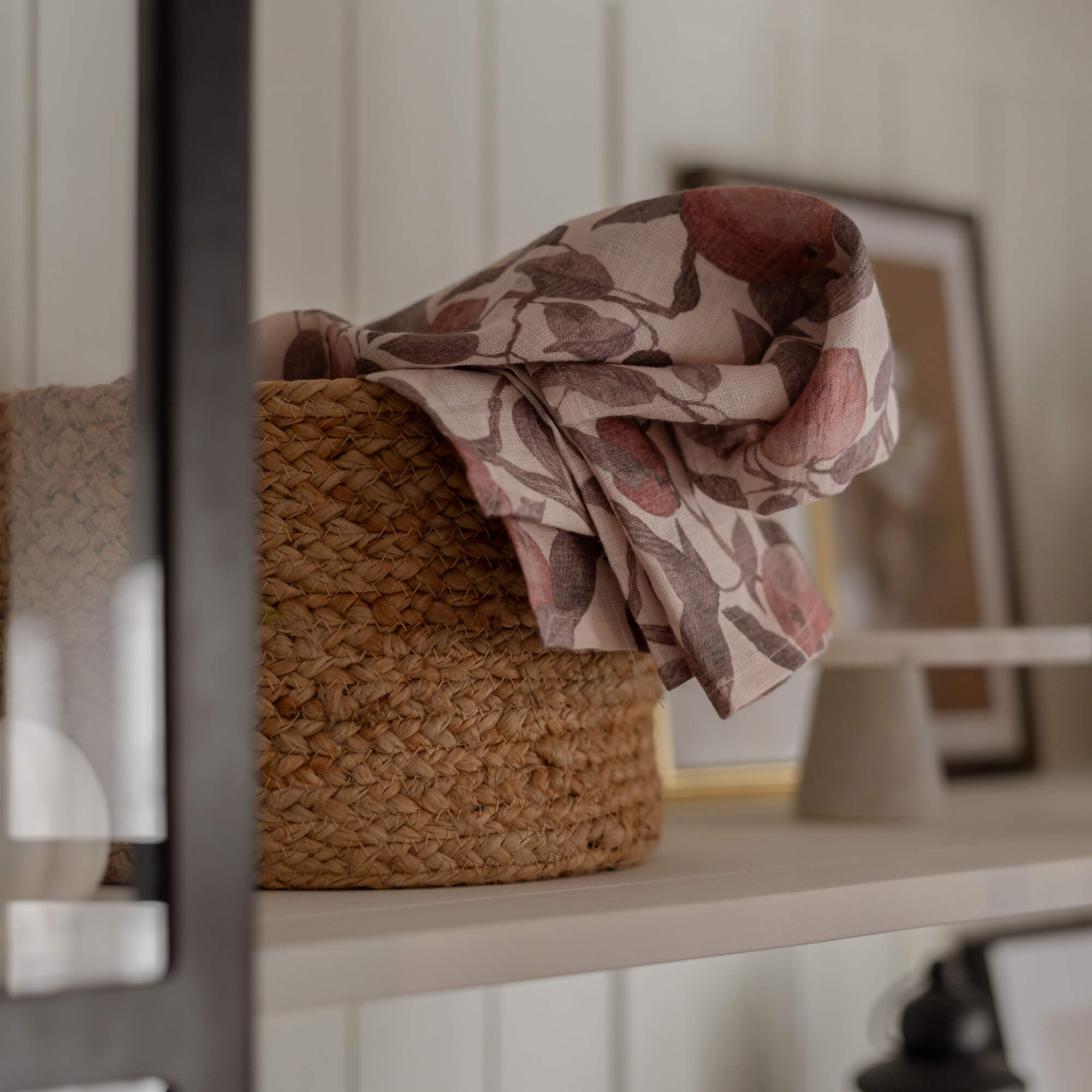 Cesta de material trenzado natural con tela de lino estampada en tonos rosas y marrones sobre estante blanco