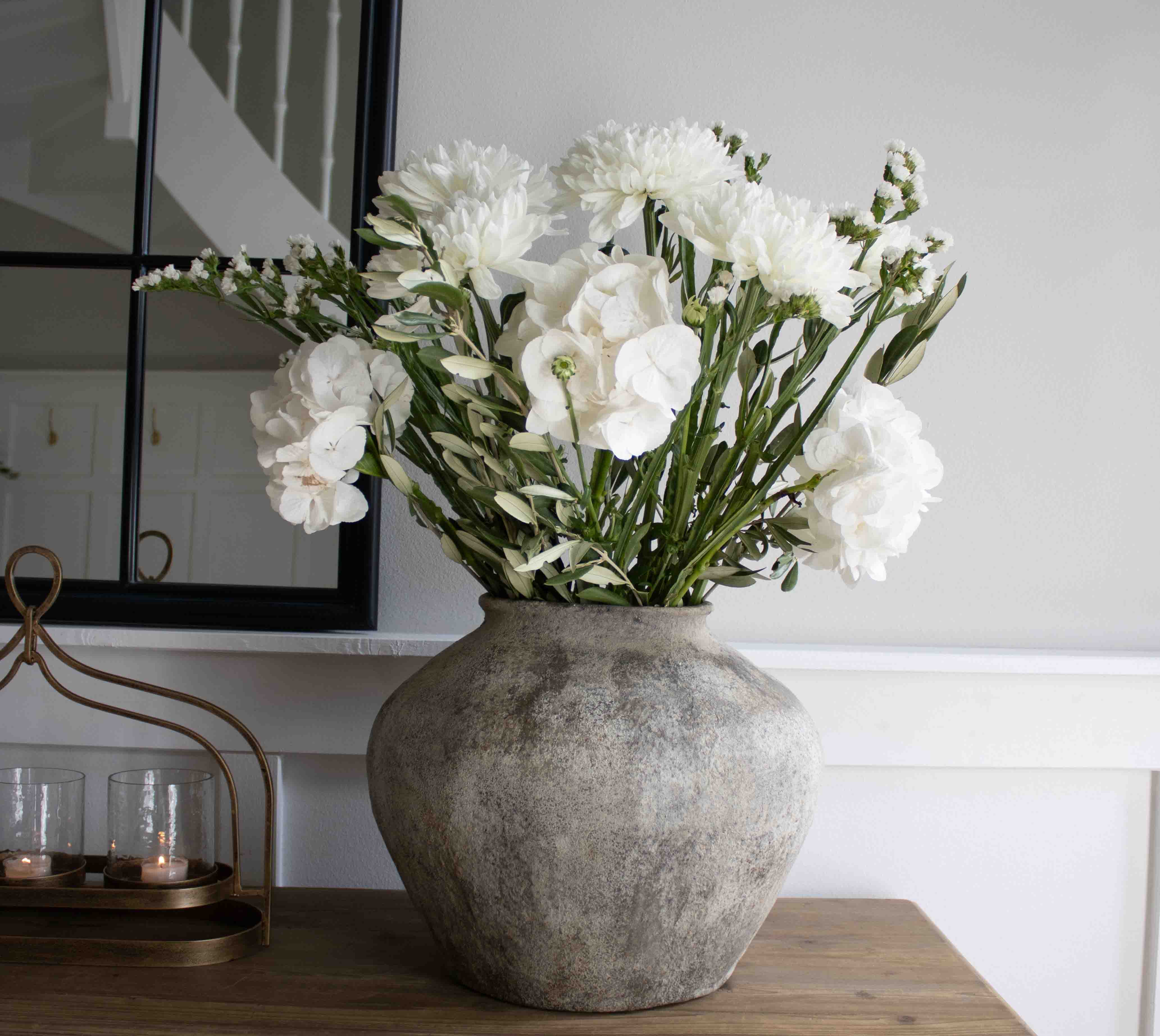 Gran jarrón de piedra gris con flores blancas decorativas sobre mesa de madera en salón
