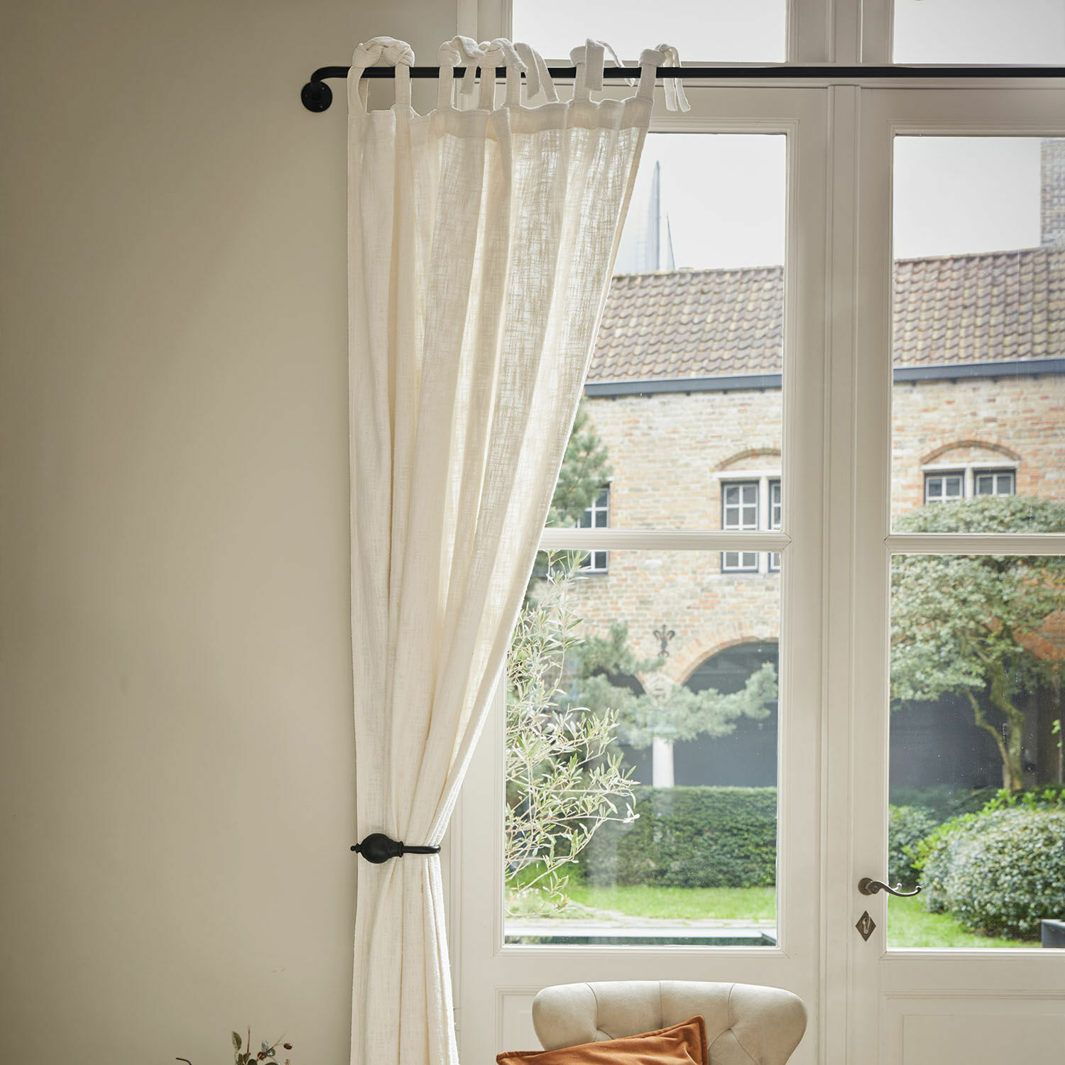 Cortina beige de lino con lazos atados en barra negra, decoración de ventana elegante