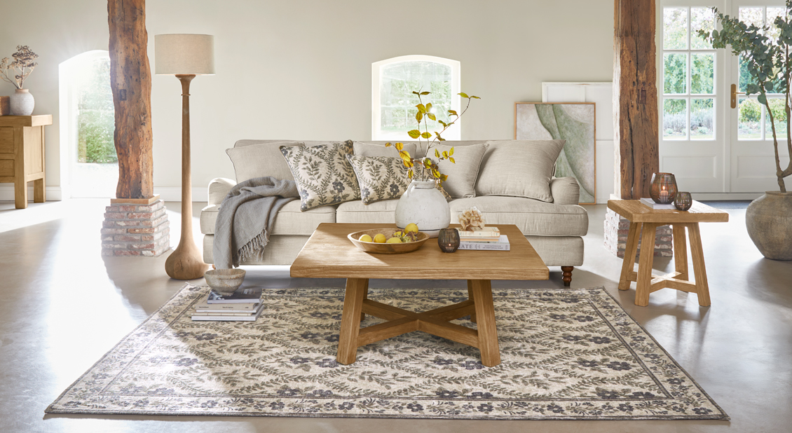 Sala acogedora con sofá beige, mesa de madera y alfombra con diseño floral en tonos naturales