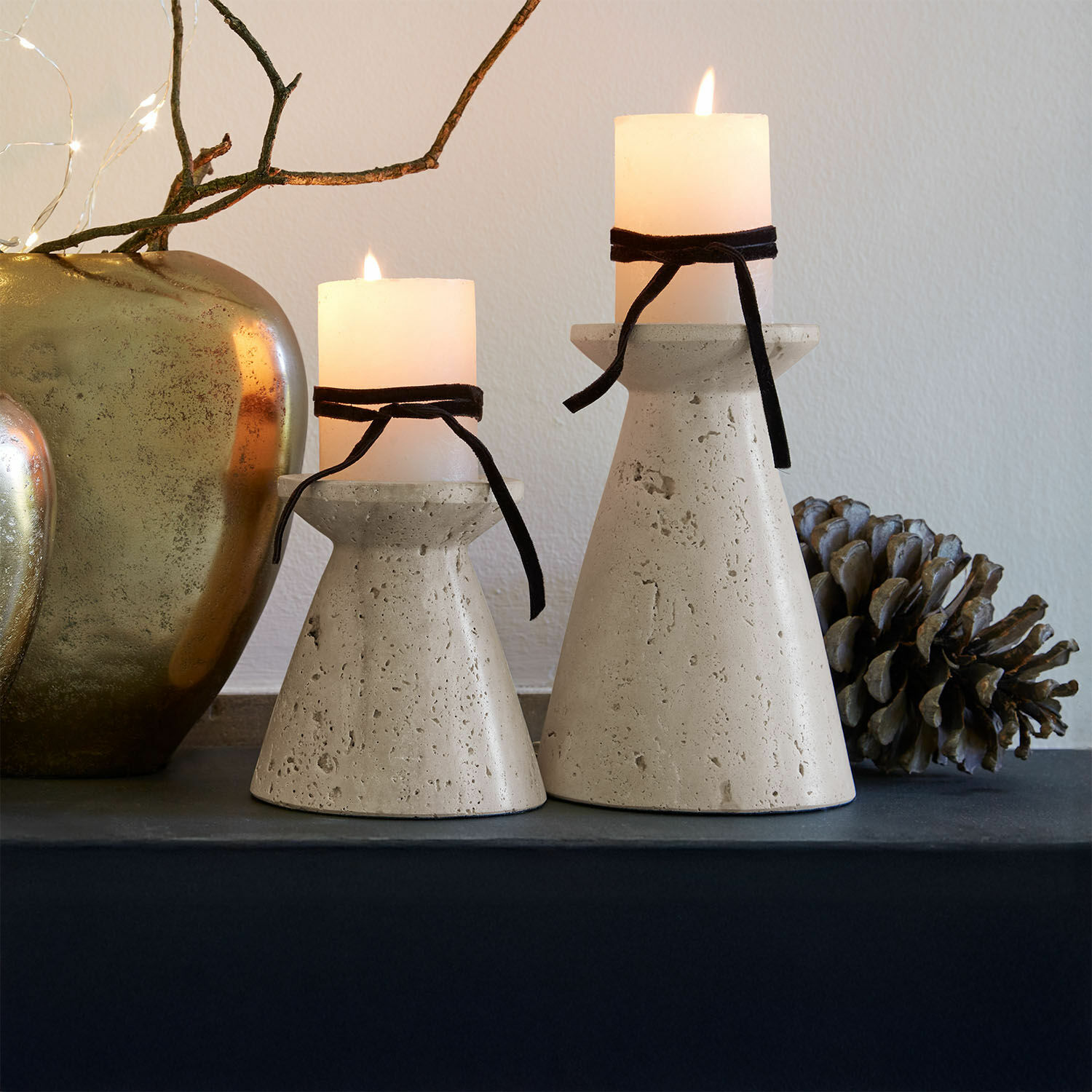 Set de 2 candeleros Bazrahim Dos candelabros de hormigón beige con velas blancas y lazos negros sobre mesa decorativa