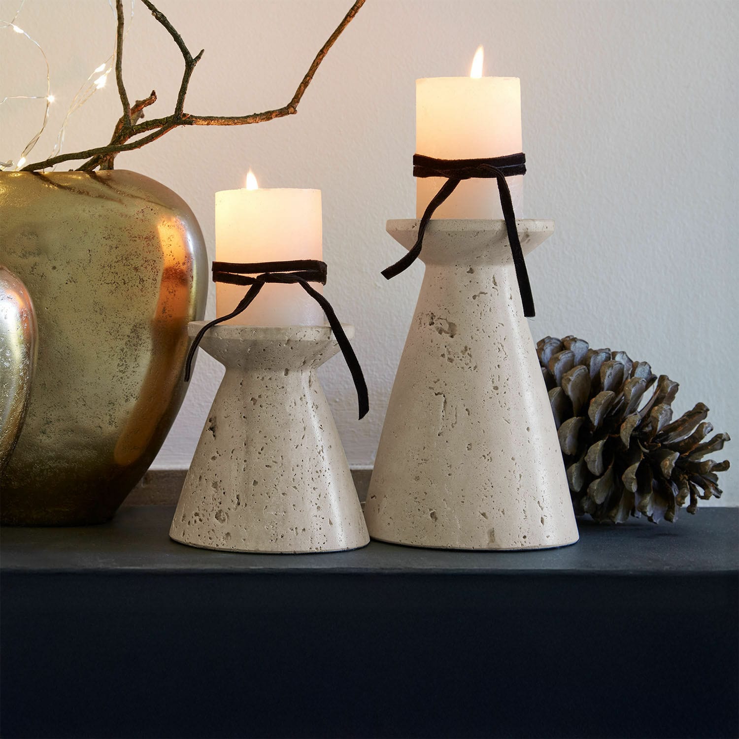 Set de 2 candeleros Bazrahim Dos candelabros de hormigón beige con velas blancas y lazos negros sobre mesa decorativa