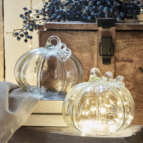 Calabazas decorativas de vidrio transparente con iluminación LED suave sobre fondo de madera rústica
