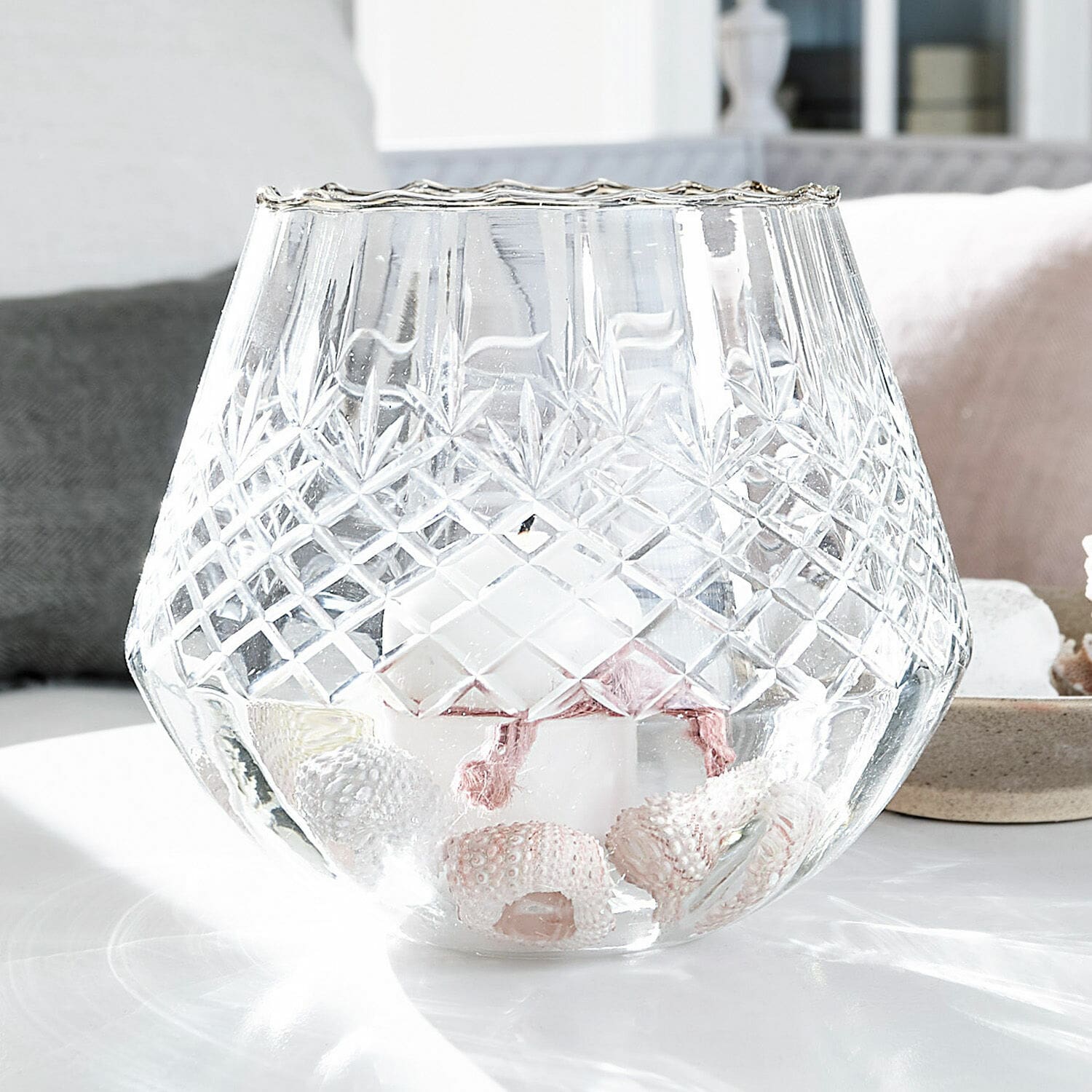 Linterna Tianie Portavelas de vidrio grabado con vela blanca y decoración de conchas sobre mesa clara