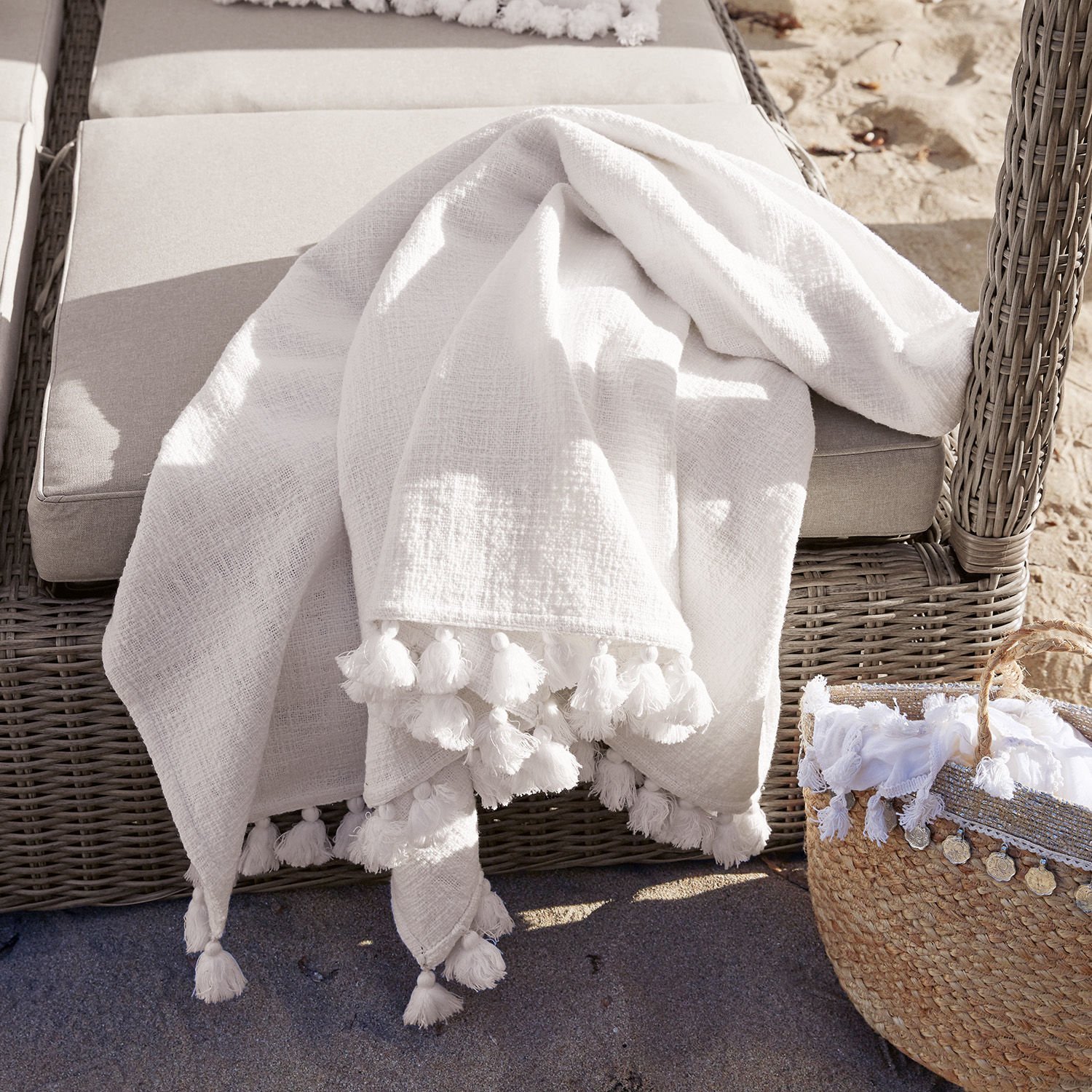 Plaid Amlamé Manta blanca de algodón con borlas sobre sillón de mimbre gris, decoración exterior de jardín