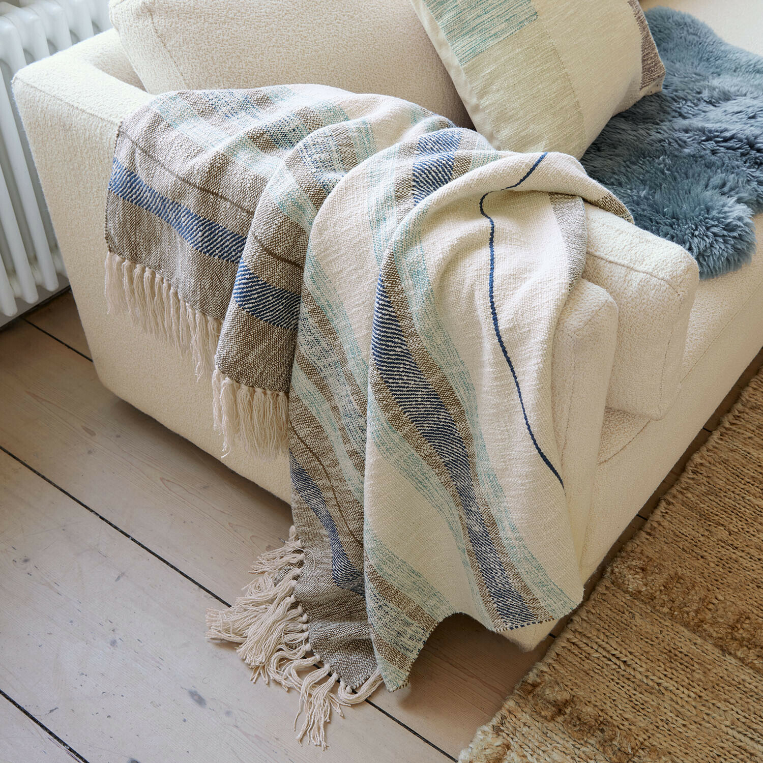 Plaid Maresas Manta suave de algodón beige con rayas azules y flecos sobre sofá crema en sala de estar