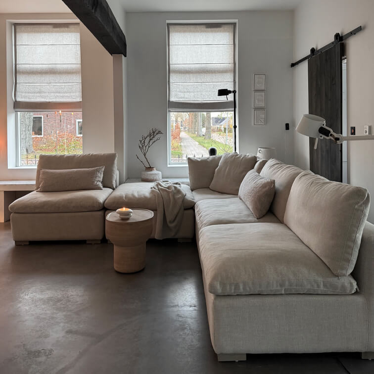 Sofá esquinero beige con cojines suaves en salón moderno con suelo de hormigón