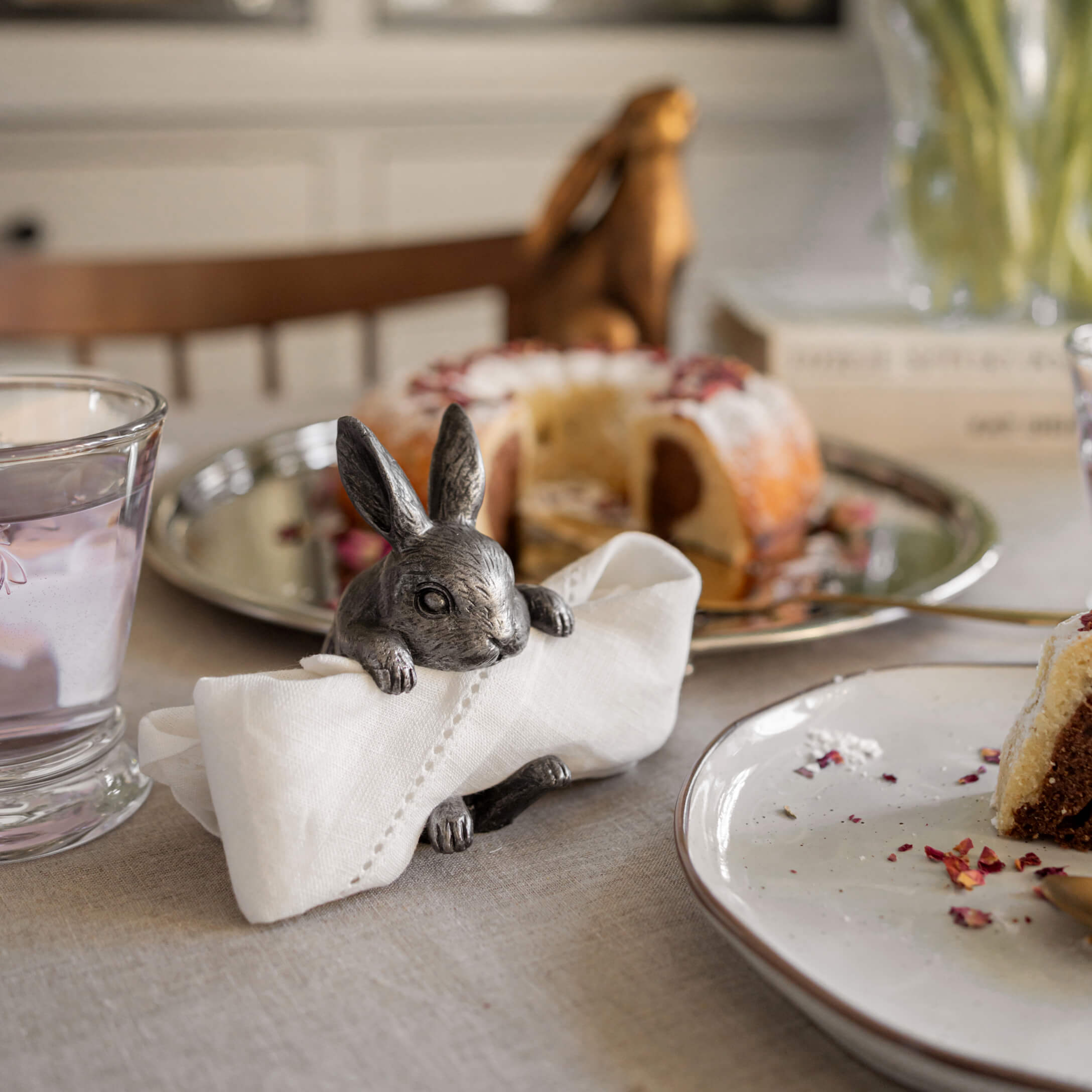 Soporte de servilletas metálico con forma de conejo sobre mesa con pastel y vaso de agua