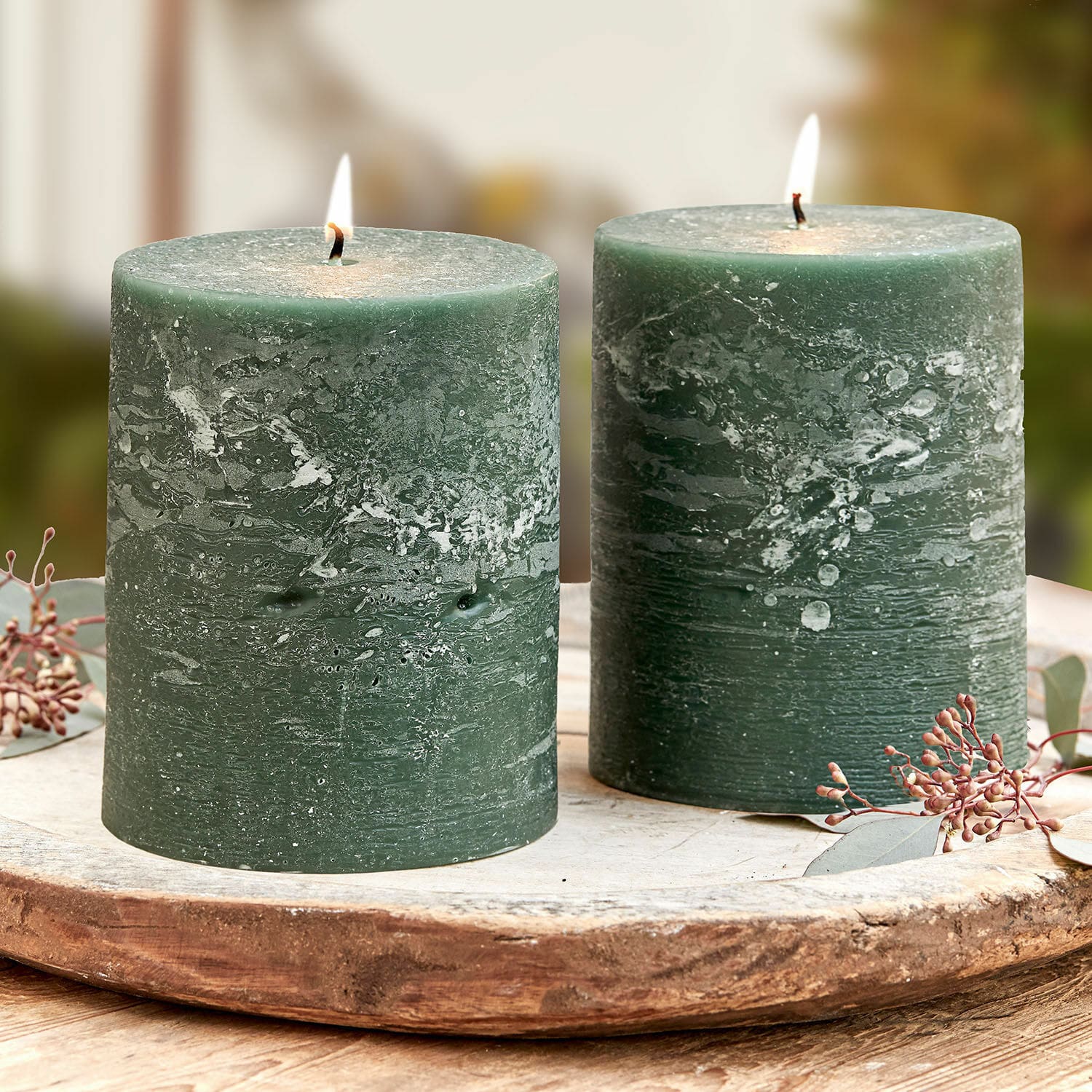 Set de 2 velas Oviedo Dos velas verdes de cera con textura rústica sobre bandeja de madera, decoración para interiores.