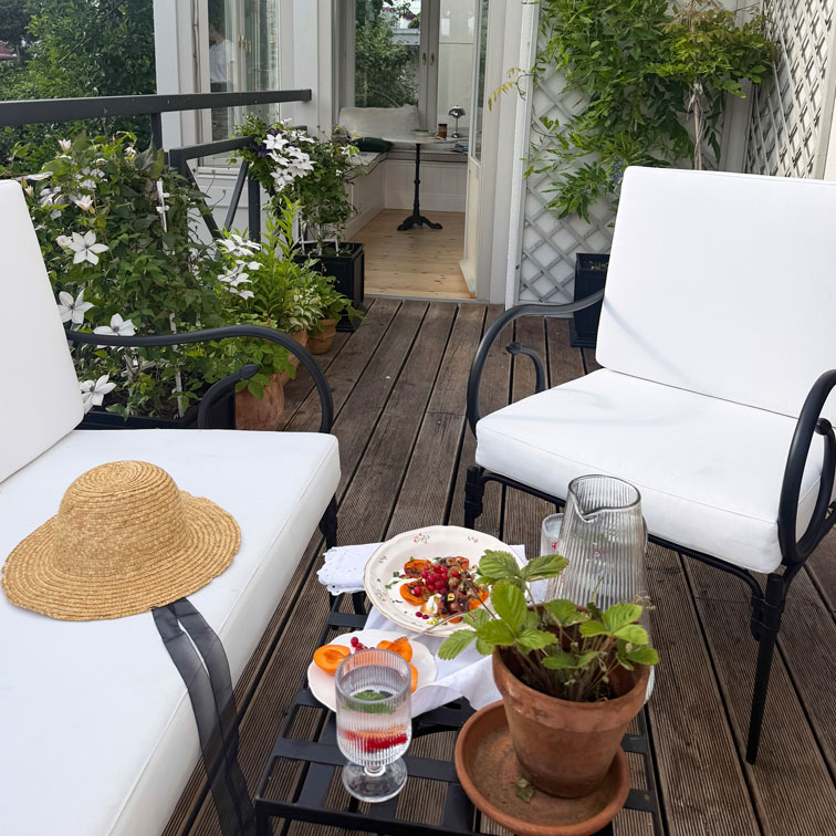 Terraza con sillas metálicas blancas, suelo de madera y plantas en macetas para zona de descanso