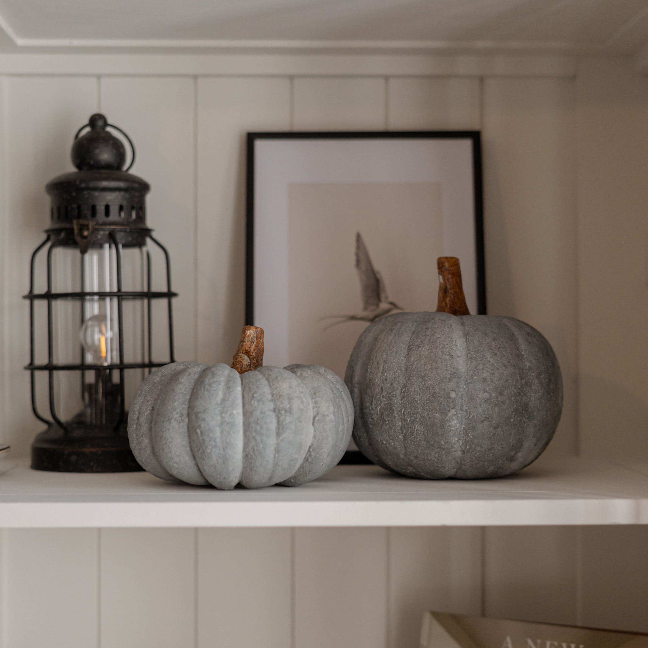 Dos calabazas decorativas grises de material similar a piedra sobre estante blanco rústico