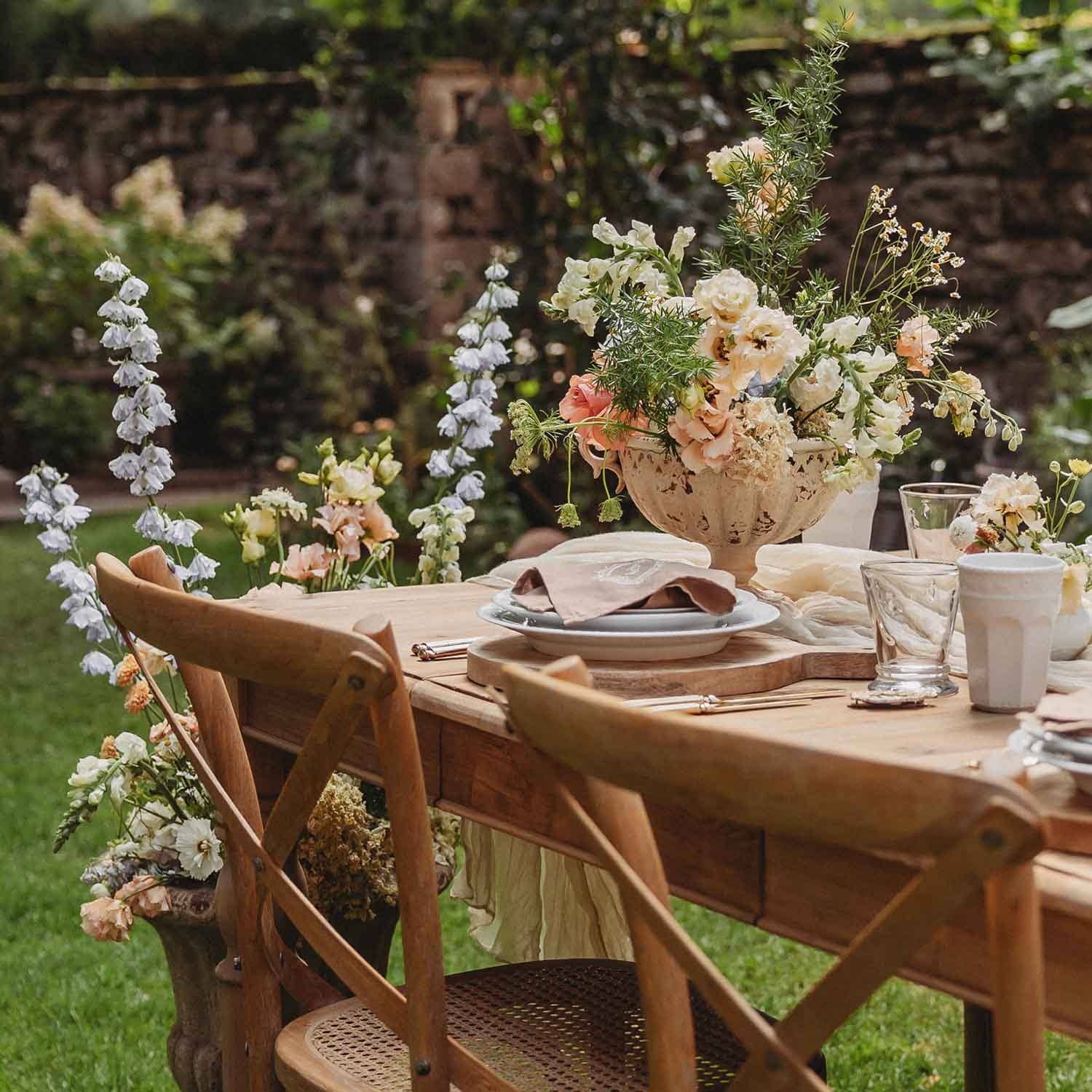 Mesa de jardín de madera con sillas rústicas y decoración floral en tonos pastel