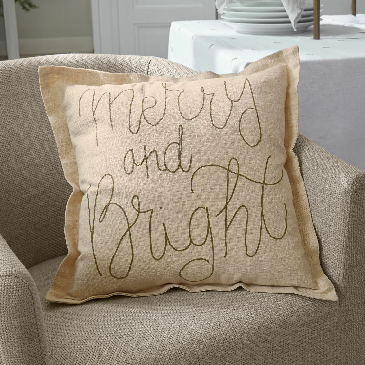 Funda de cojín Torvenna Cojín decorativo beige de lino con texto Merry and Bright sobre sillón beige, decoración de interiores