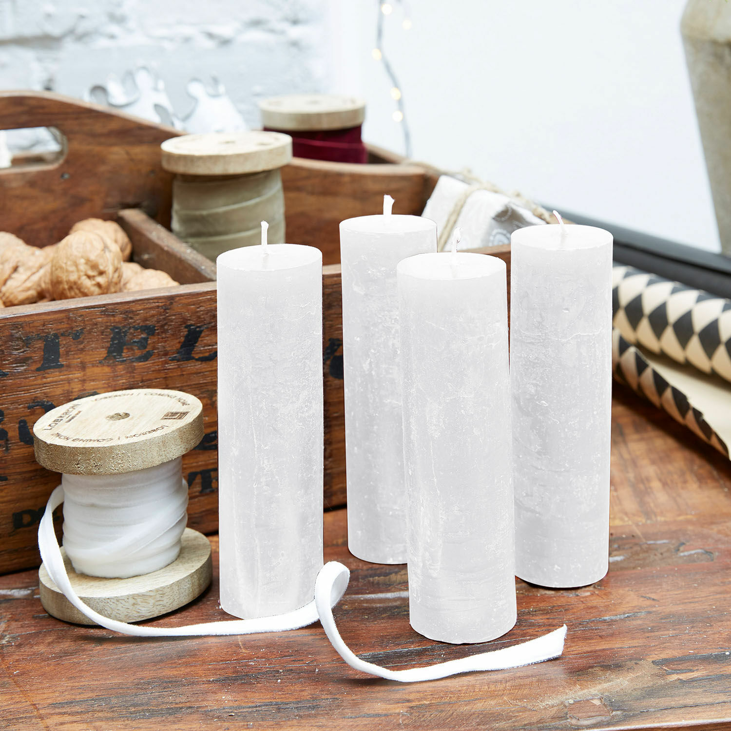 Set de 4 velas Muriel Conjunto de cuatro velas blancas de cera natural sobre mesa de madera con decoraciones