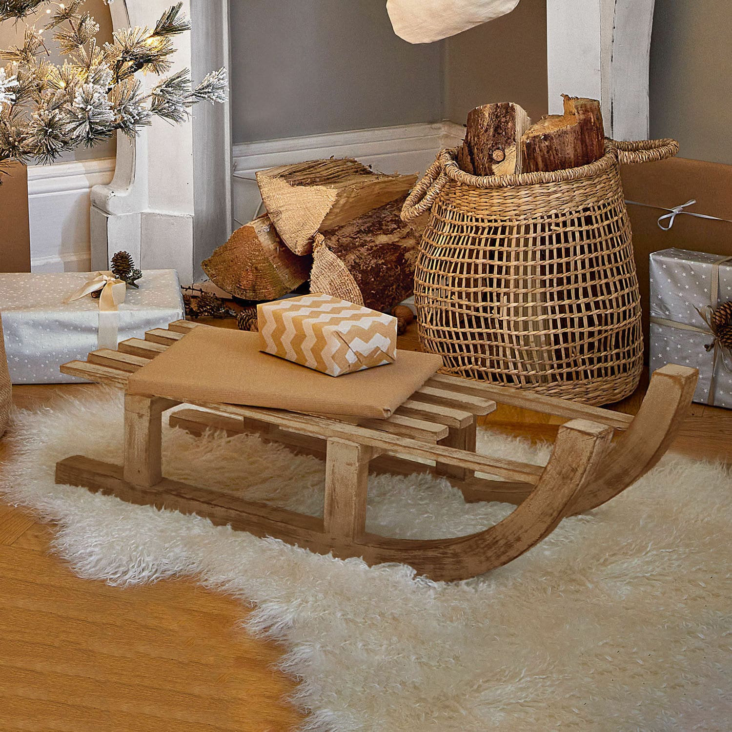 Trineo decorativo FSC®-100% Hoekstra Trineo decorativo de madera sobre alfombra blanca de piel sintética con regalos y cesta de leña
