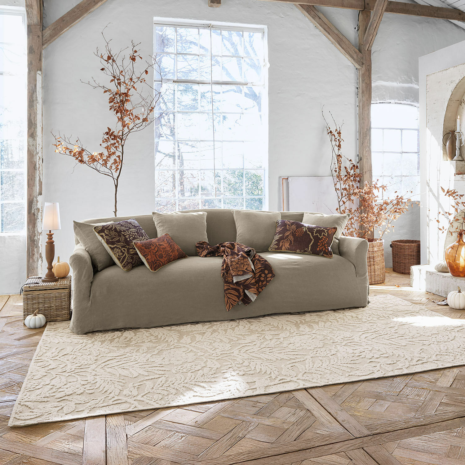 Alfombra Azimra Sofá beige de tela en sala luminosa con cojines decorativos y alfombra con diseño de hojas