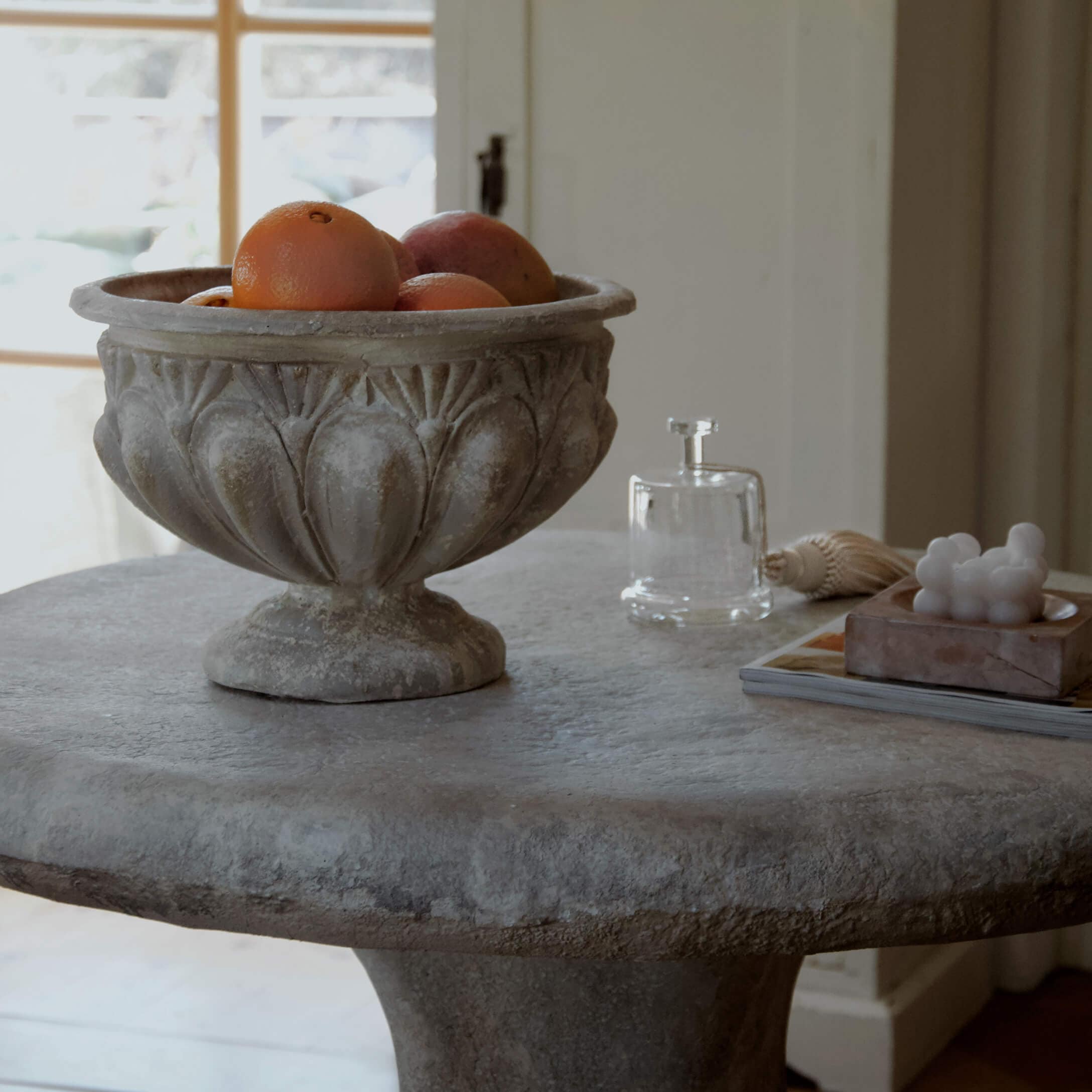 Cuenco decorativo de piedra con naranjas sobre mesa de piedra en interior luminoso