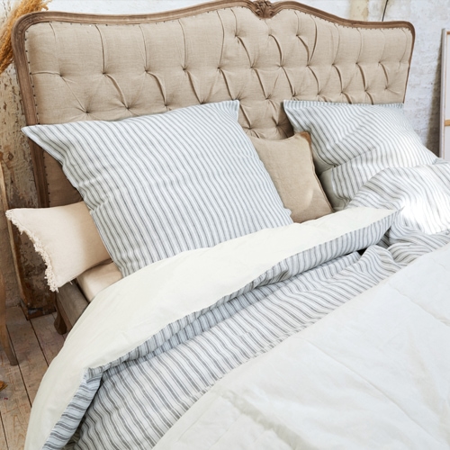 Cabecero acolchado beige con ropa de cama a rayas grises y edredón crema en dormitorio acogedor