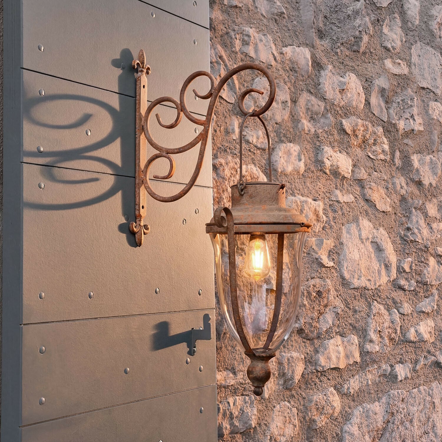 Farol solar Volanaïs Lámpara de pared exterior de metal oxidado con cristal transparente montada en pared de piedra iluminada