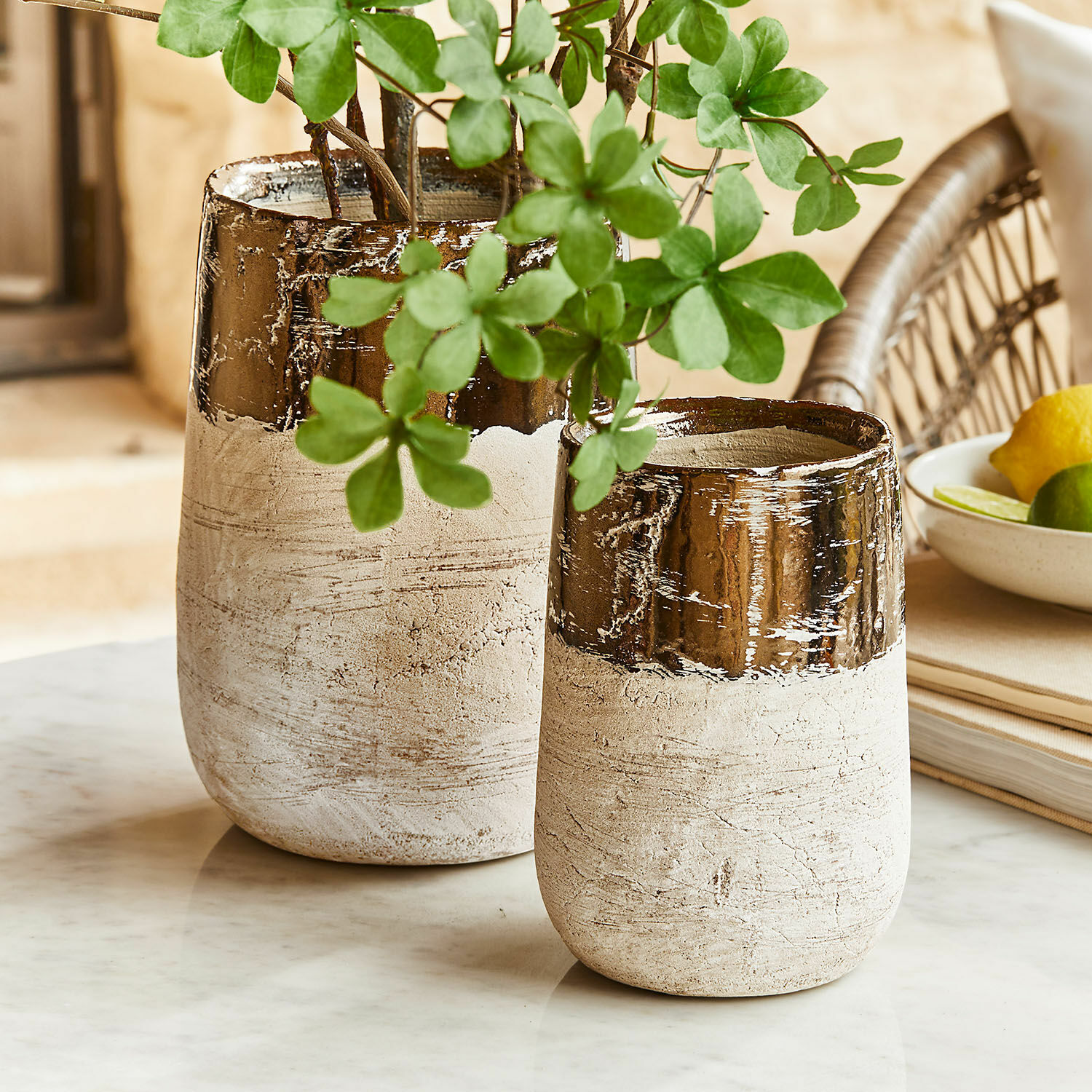 Set de 2 jarrones Hafira Dos jarrones de cerámica beige y marrón sobre mesa de mármol con hojas verdes