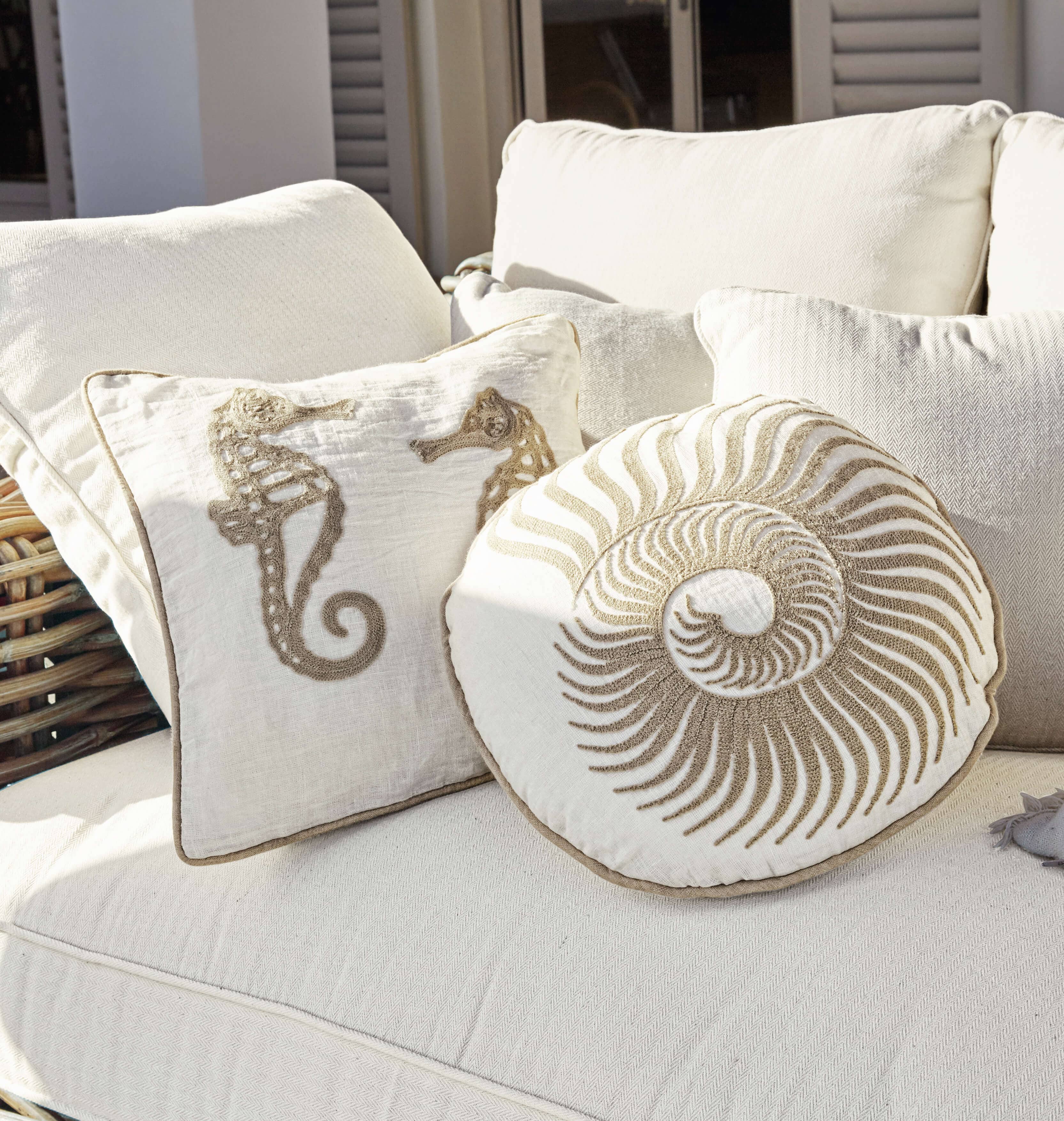 Cojines decorativos beige con motivos marinos sobre sofá claro, textiles para el hogar