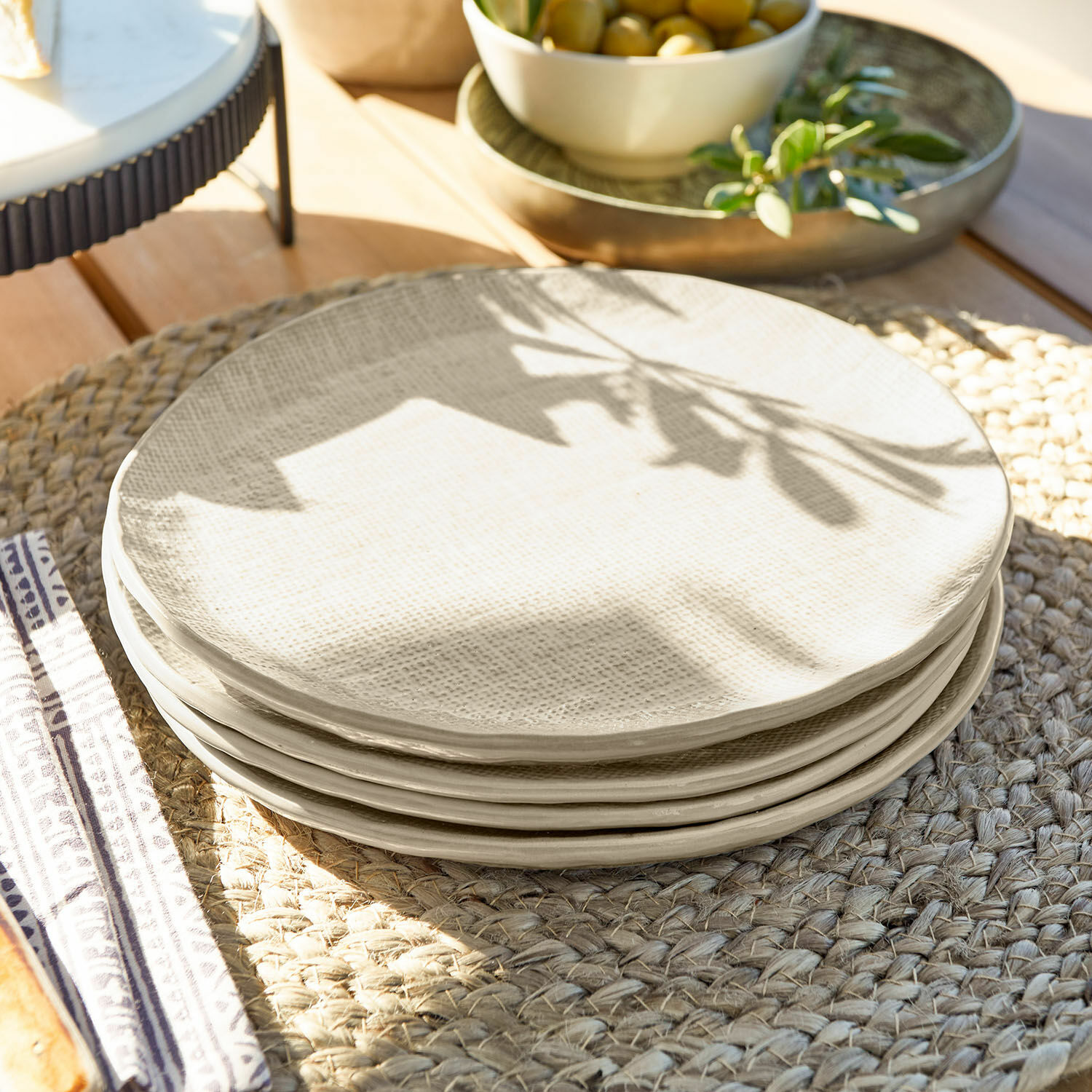 Set de 4 platos de postre Luganville Juego de platos de cerámica crema con textura sobre un salvamanteles trenzado de madera
