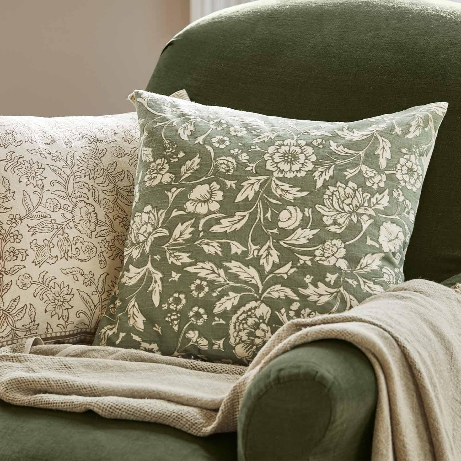 Cojín verde con estampado floral blanco sobre sillón verde con manta beige para decoración