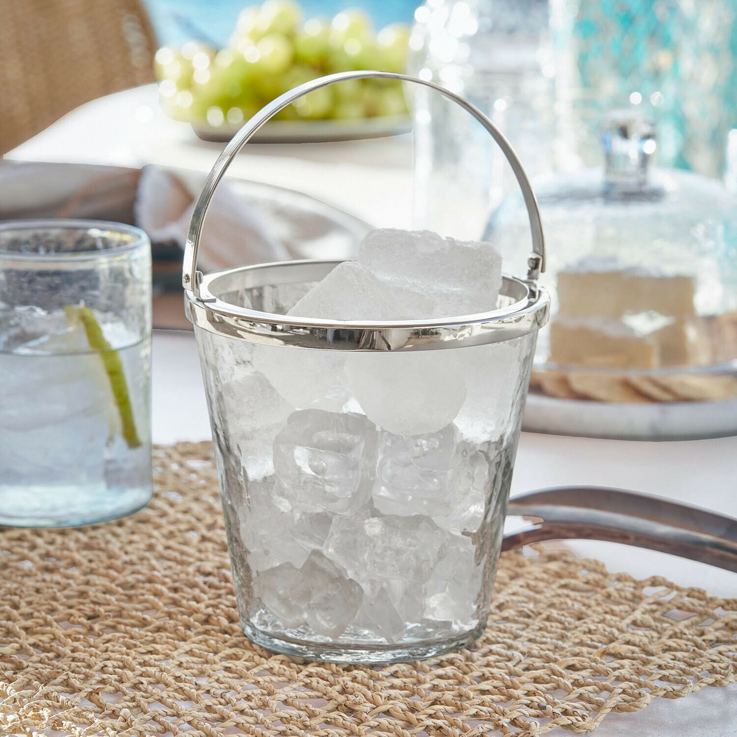 Cubo de hielo de vidrio con asa metálica sobre la mesa, ideal para servir bebidas con hielo