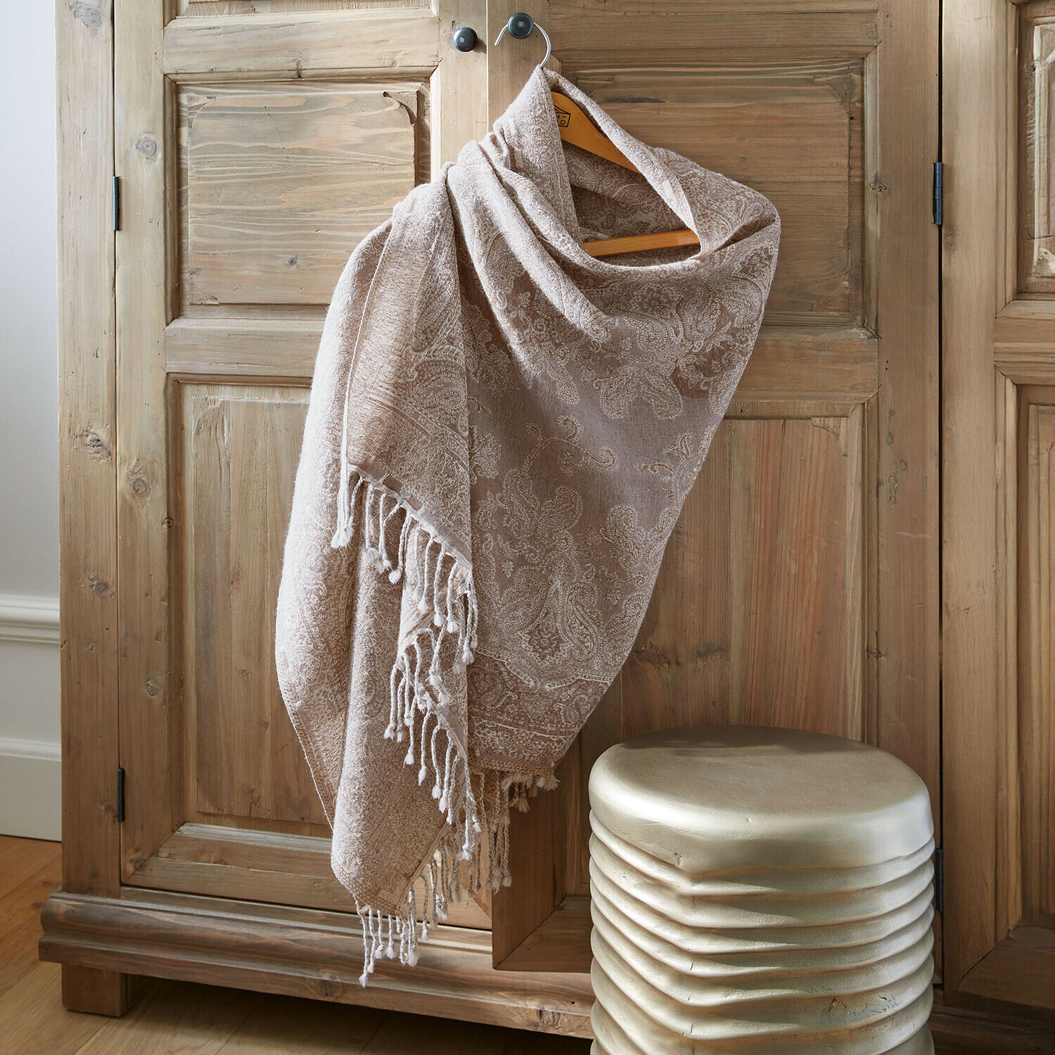 Chal beige con diseño paisley y flecos colgado en armario de madera, tejido suave y accesorio decorativo