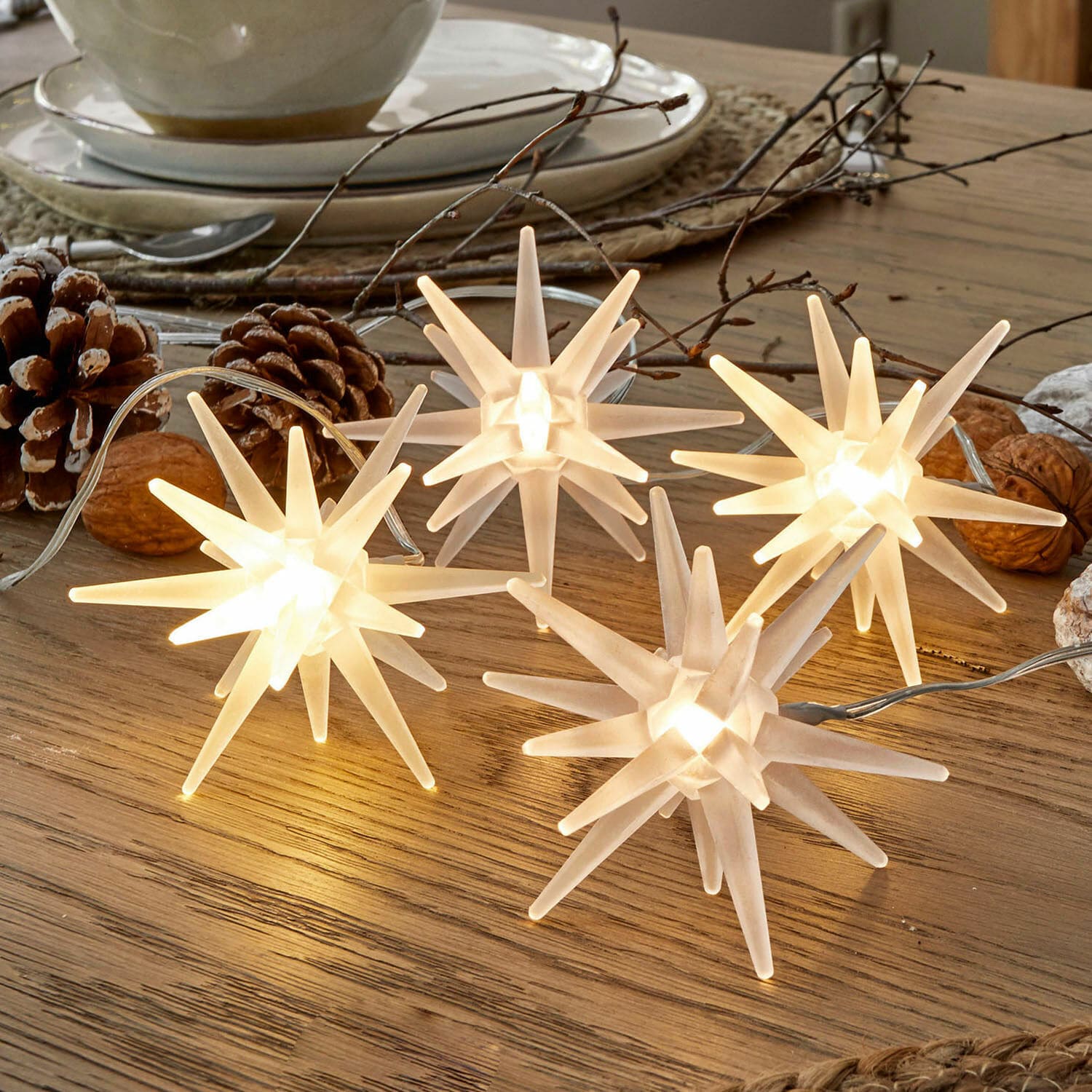 Set de 4 estrellas LED Ciseau Guirnalda de luces decorativas en forma de estrellas blancas de plástico sobre mesa de madera con adornos naturales