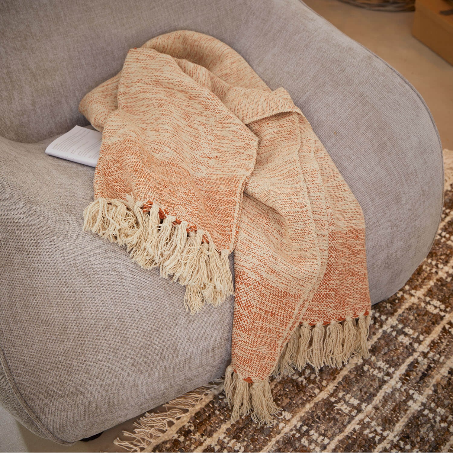 Manta beige y naranja con flecos sobre sofá gris, tejido suave para decoración del hogar