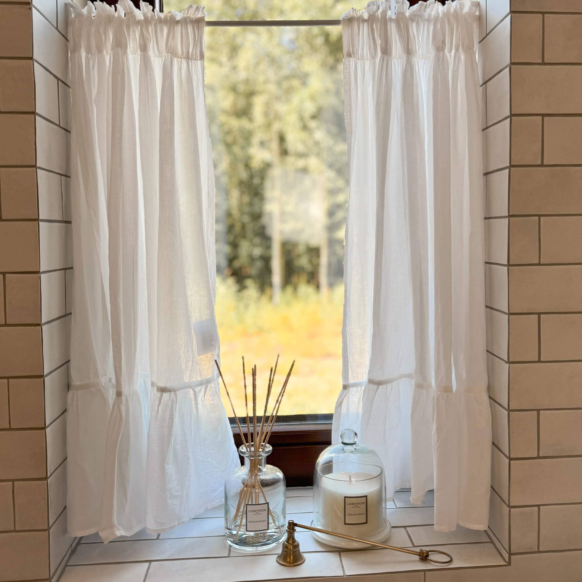 Cortinas blancas de lino en ventana con vela decorativa y difusor de aroma en el alféizar